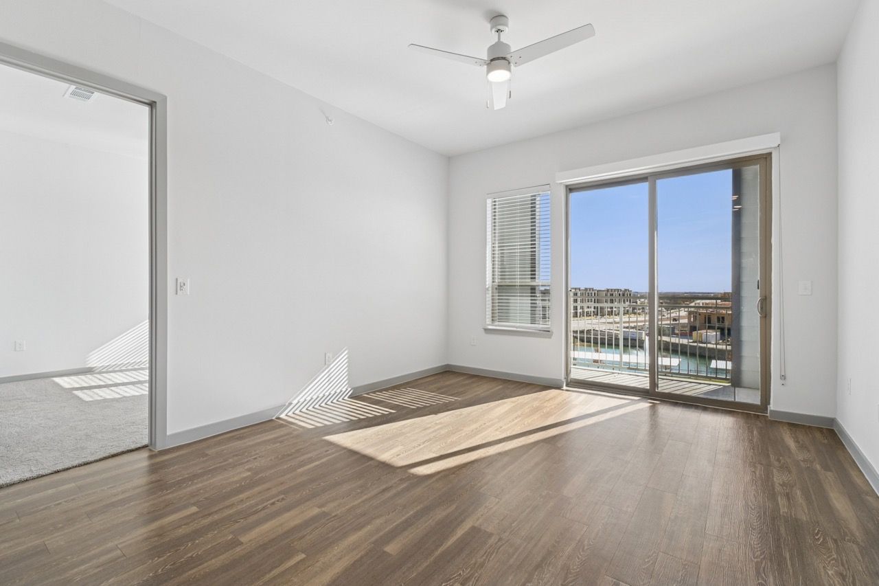 Empty living room with wood-look flooring, white walls, a ceiling fan, and a sliding door to the balcony.