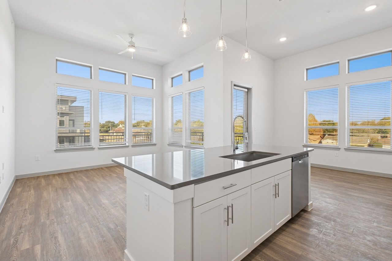 Bright open kitchen with white cabinets, a large central island, and a stainless steel sink beneath expansive windows.