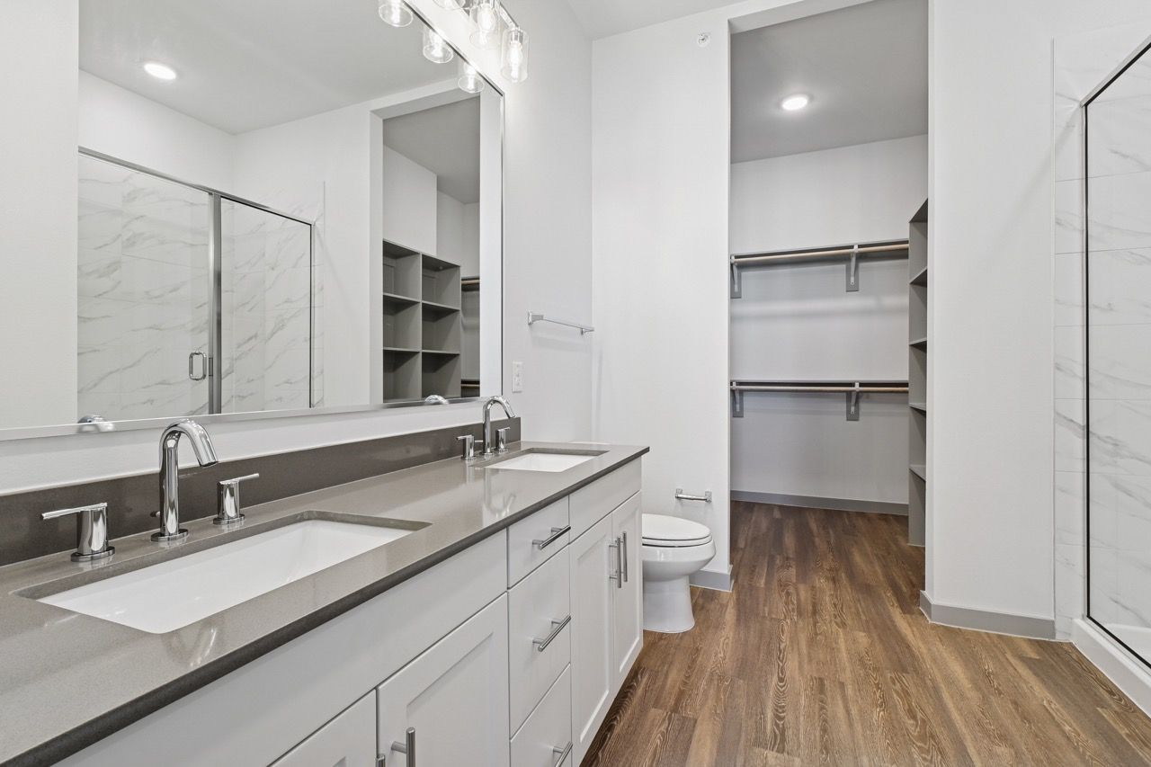 Modern bathroom with double vanity, large mirror, and walk-in closet in a bright apartment.