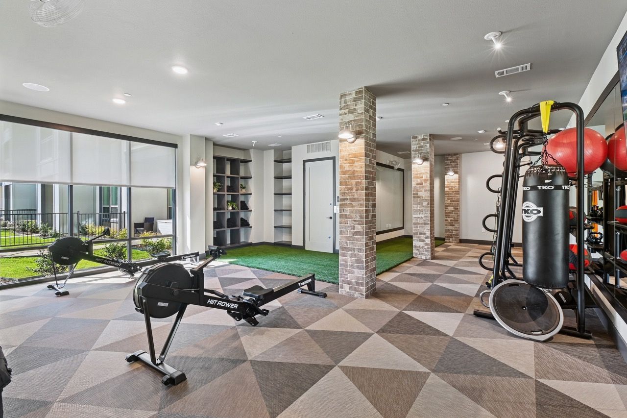 Apartment community fitness center with cardio machines, a punching bag, weights, and brick columns.