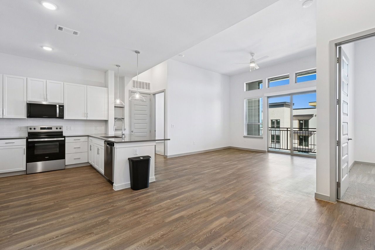 Open kitchen and living area with white cabinets, stainless-steel appliances, island, and large windows.