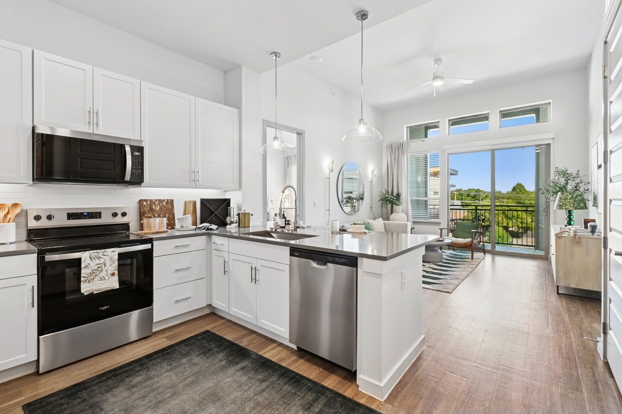 Bright white kitchen with stainless steel appliances and an island, open to living area with balcony.