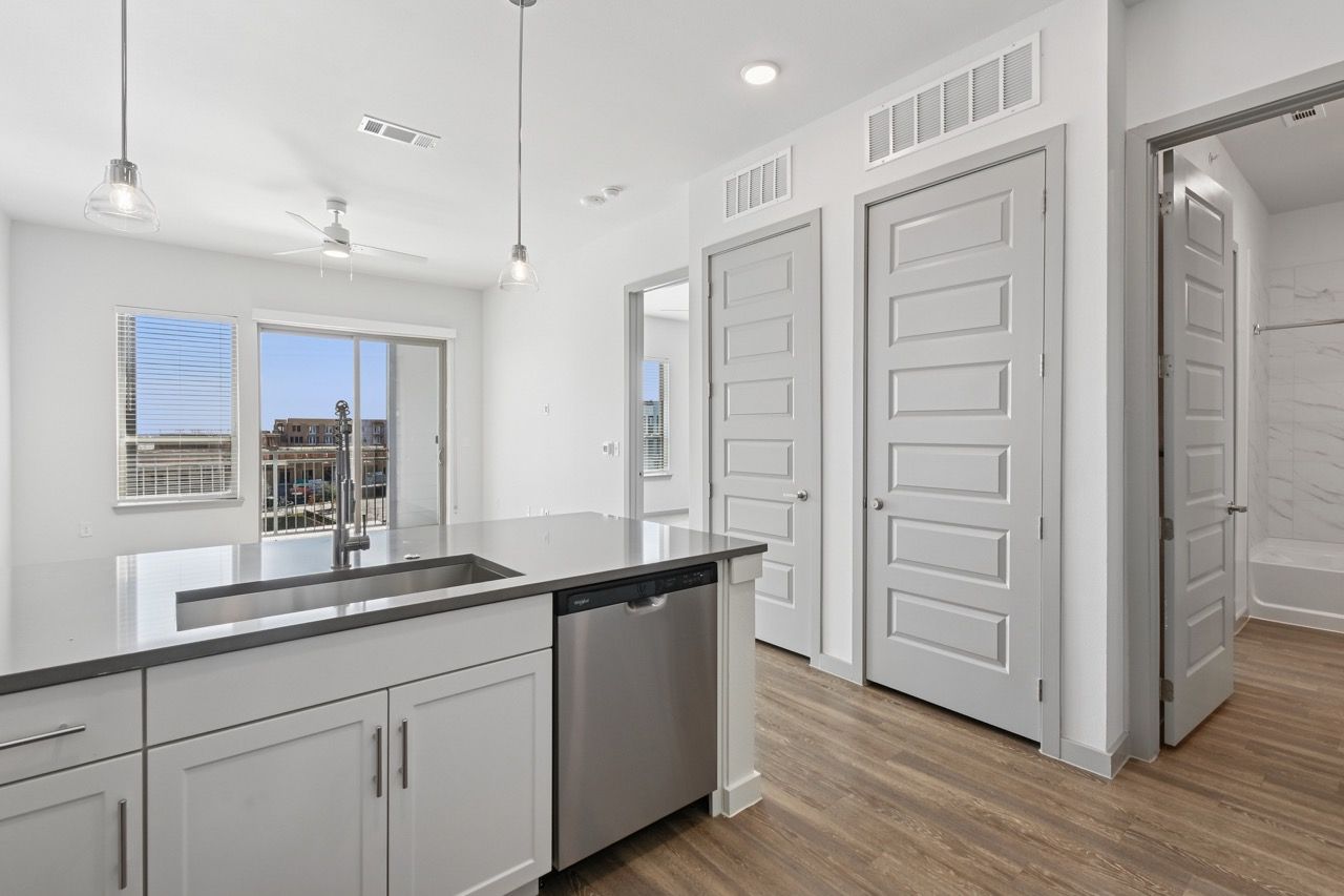 Open-concept kitchen in a bright apartment with an island, stainless dishwasher, and balcony door.