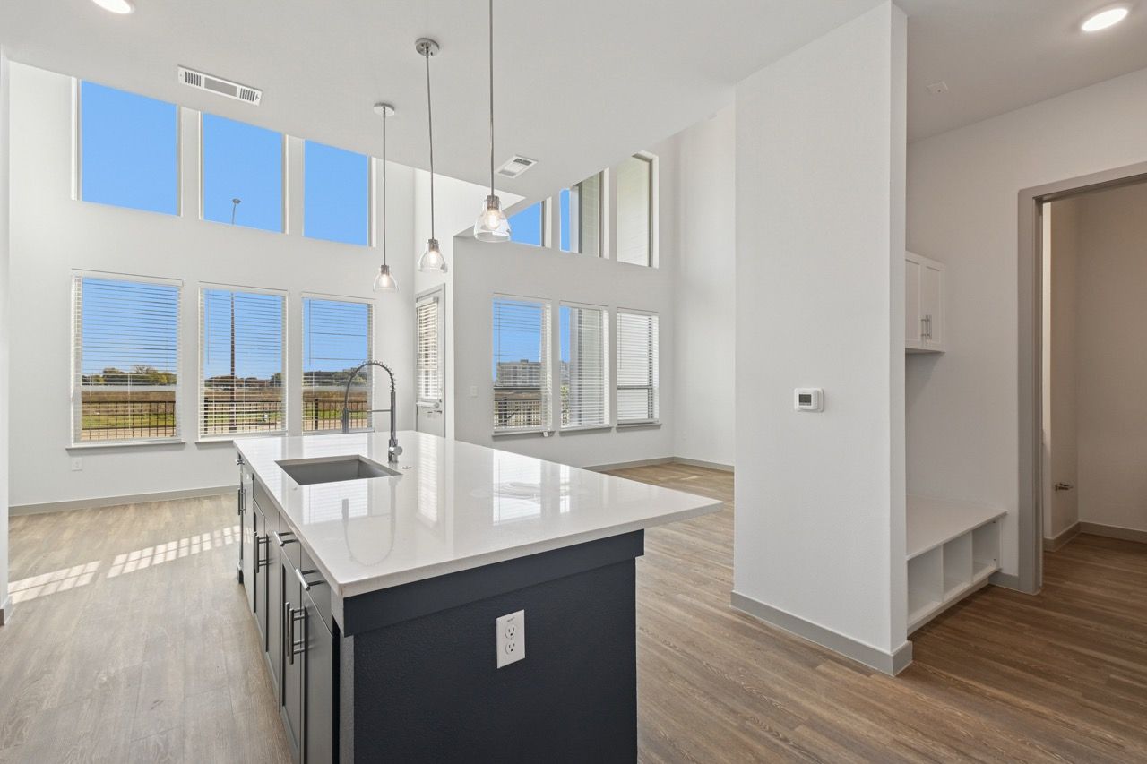 Open-concept kitchen with a large white island, sink, pendant lights, and tall bright windows.