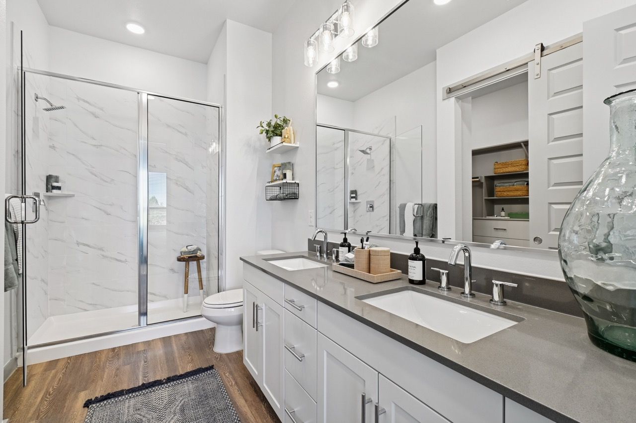 Modern bathroom with dual sinks, glass-enclosed shower, white cabinets, and a large mirror.