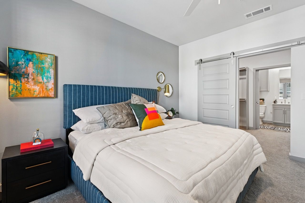 Bedroom with blue upholstered bed, white bedding, nightstand, and doorway to bathroom.
