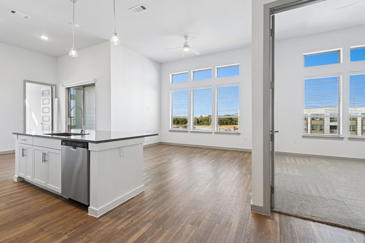 Open-concept kitchen with island, sink, stainless dishwasher, and large windows in a bright living area.