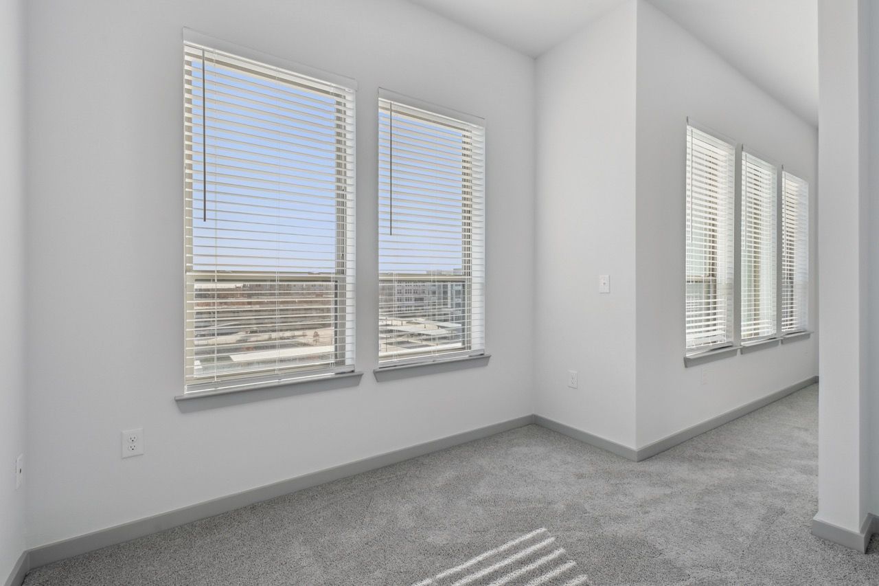 Bright empty apartment room with large windows and white blinds.