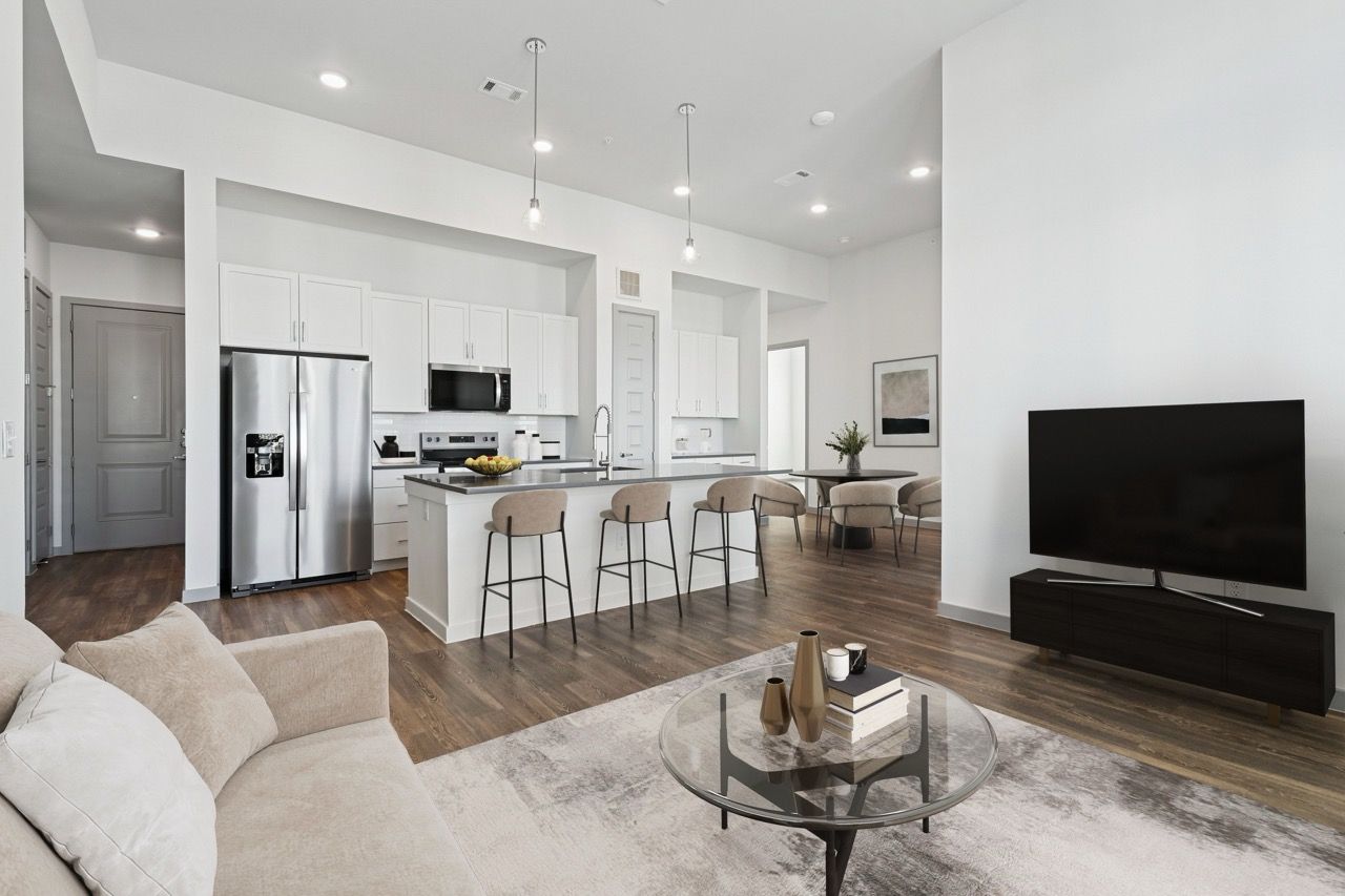 Open-concept apartment living area with a kitchen island, white cabinets, stainless appliances, and a TV.