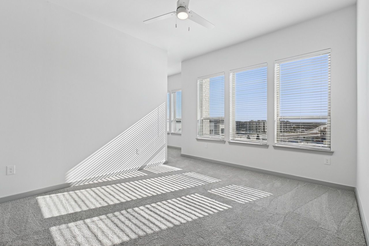 Bright empty apartment room with multiple windows and a ceiling fan.