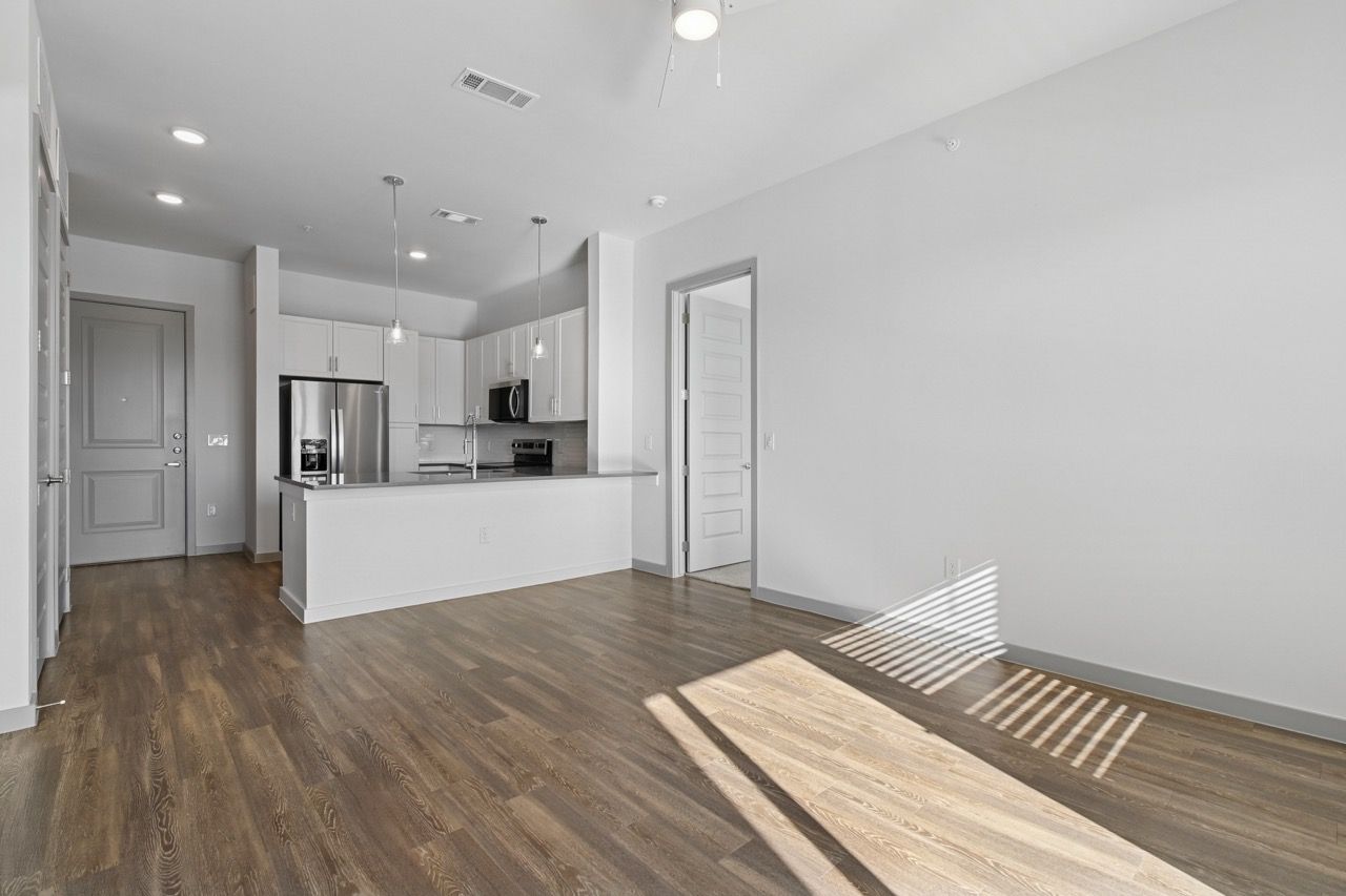 Open-concept apartment living area with white kitchen cabinets, stainless steel appliances, and hardwood floors.