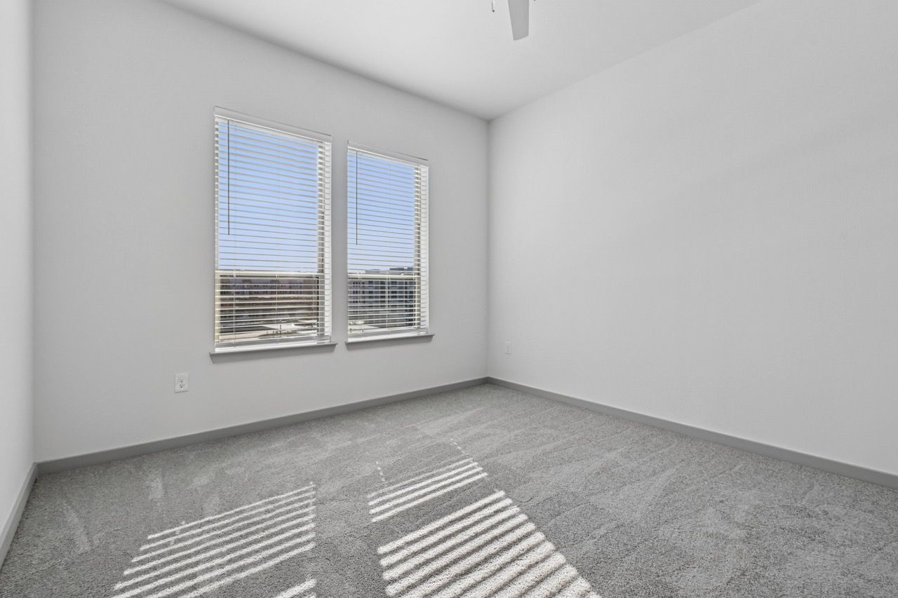 Empty bedroom in a modern apartment with two windows and blinds.