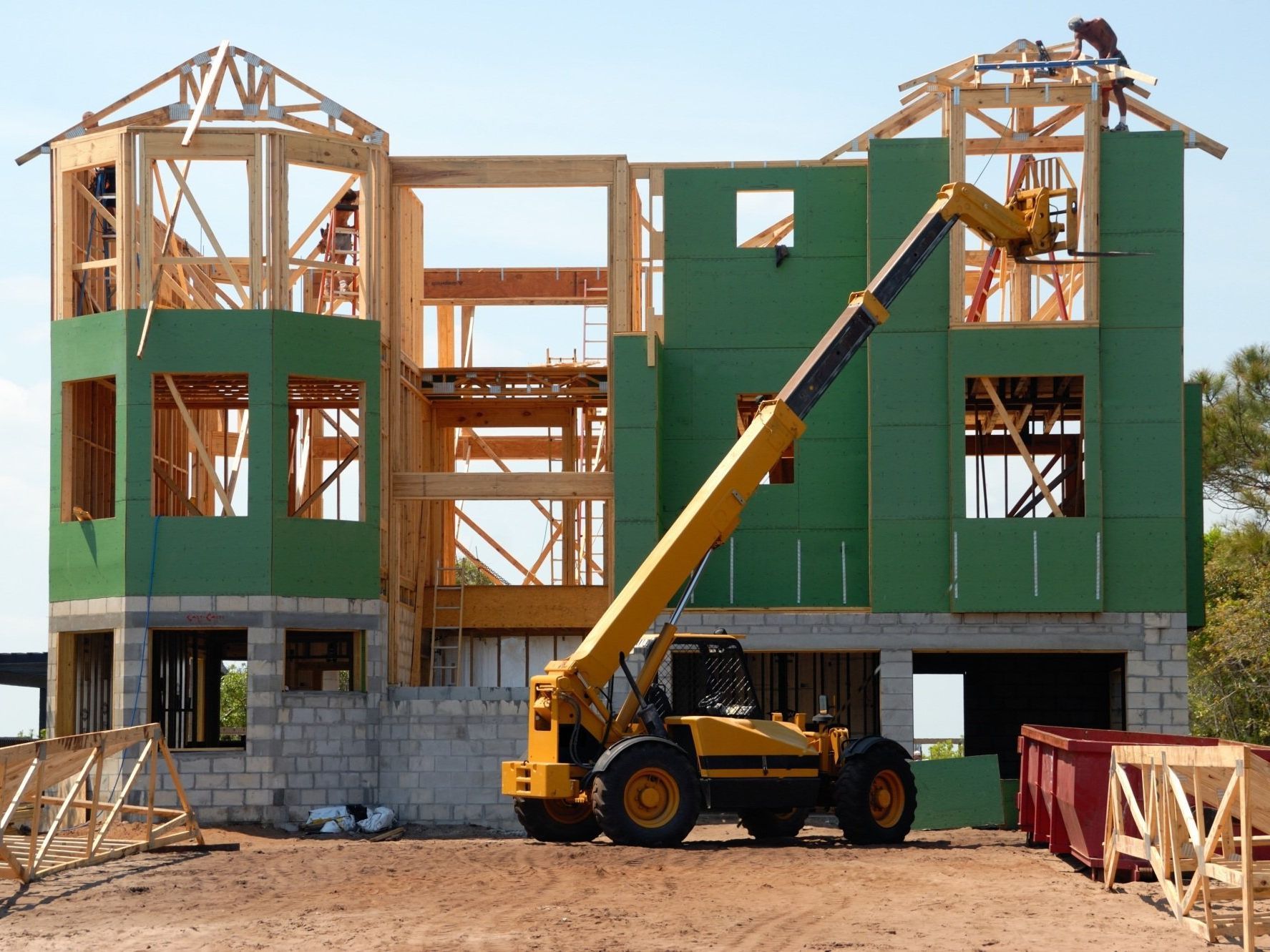 A yellow forklift is parked in front of a house under construction