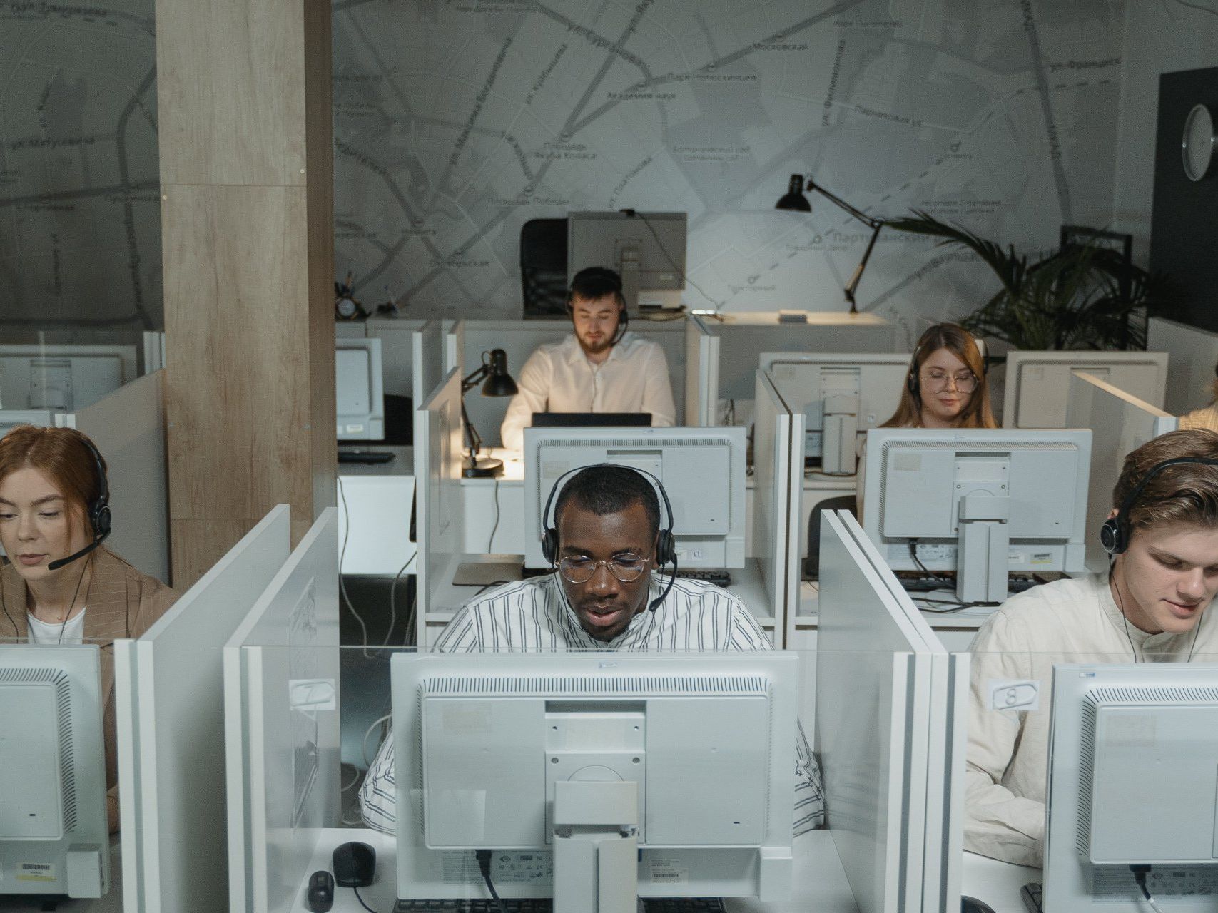 A group of people are sitting in front of computer monitors in a call center.