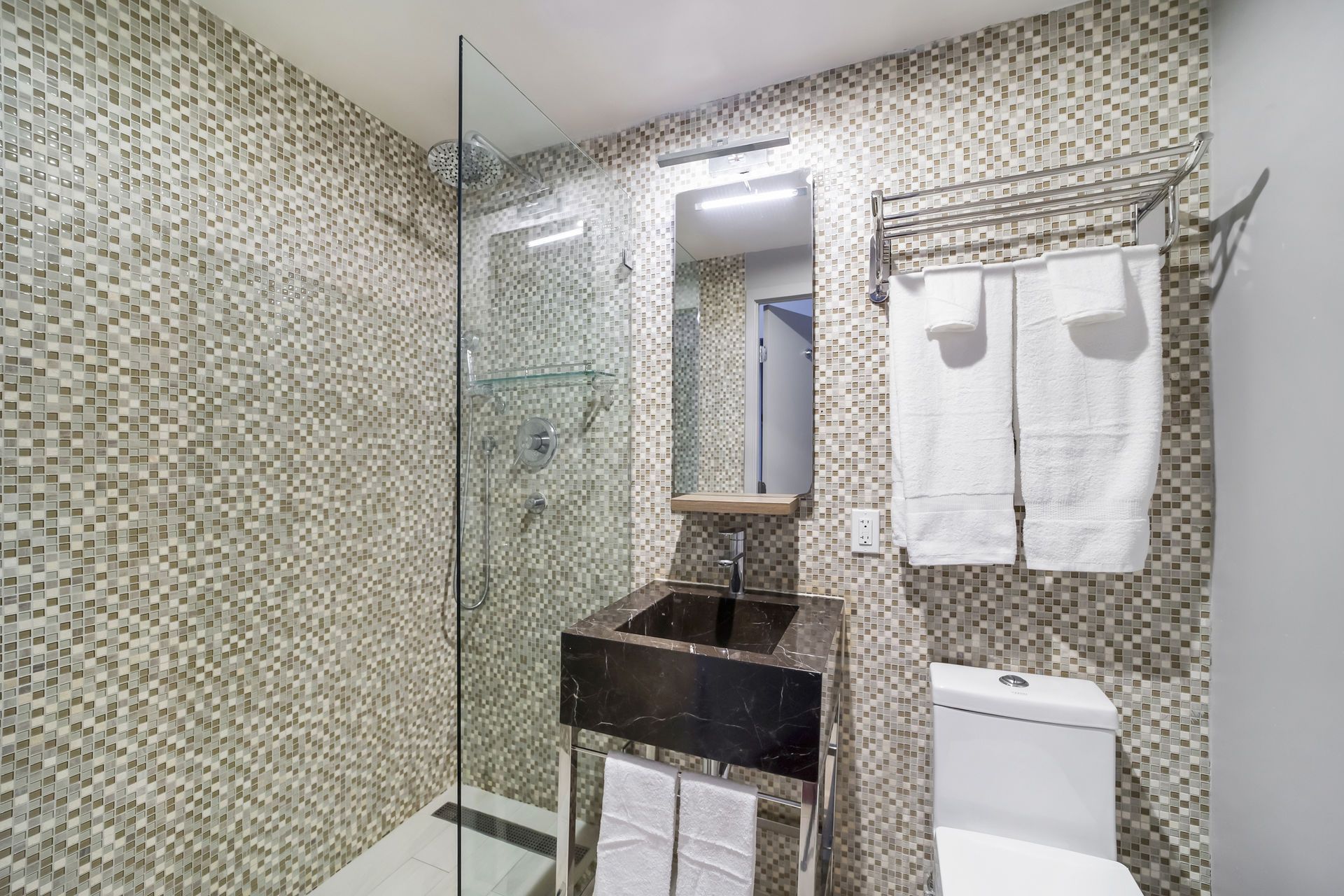 Small bathroom with mosaic tile walls, a glass shower, black sink, and white towels.