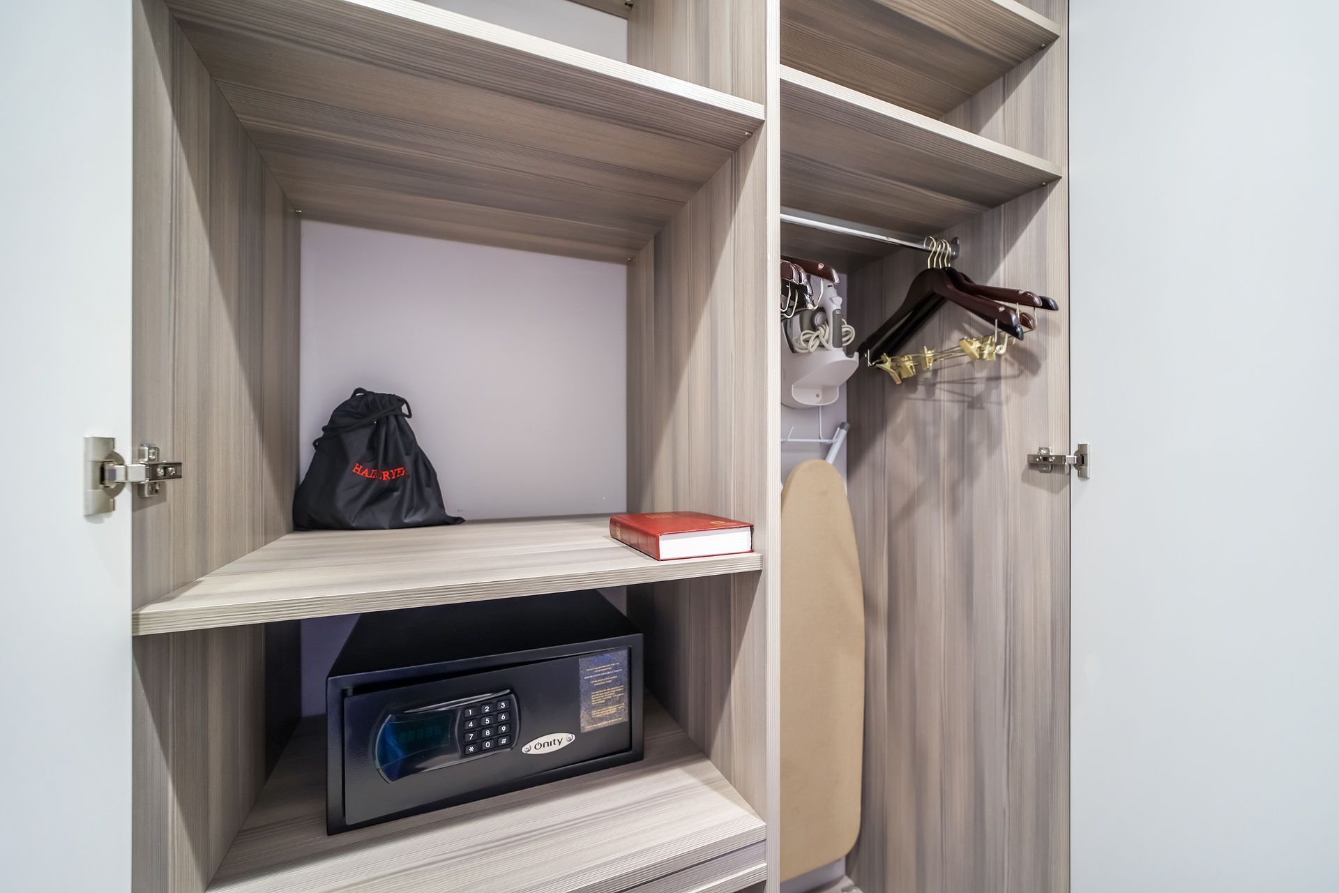Closet with shelves, a safe, a bag, a book, hangers, and an ironing board.