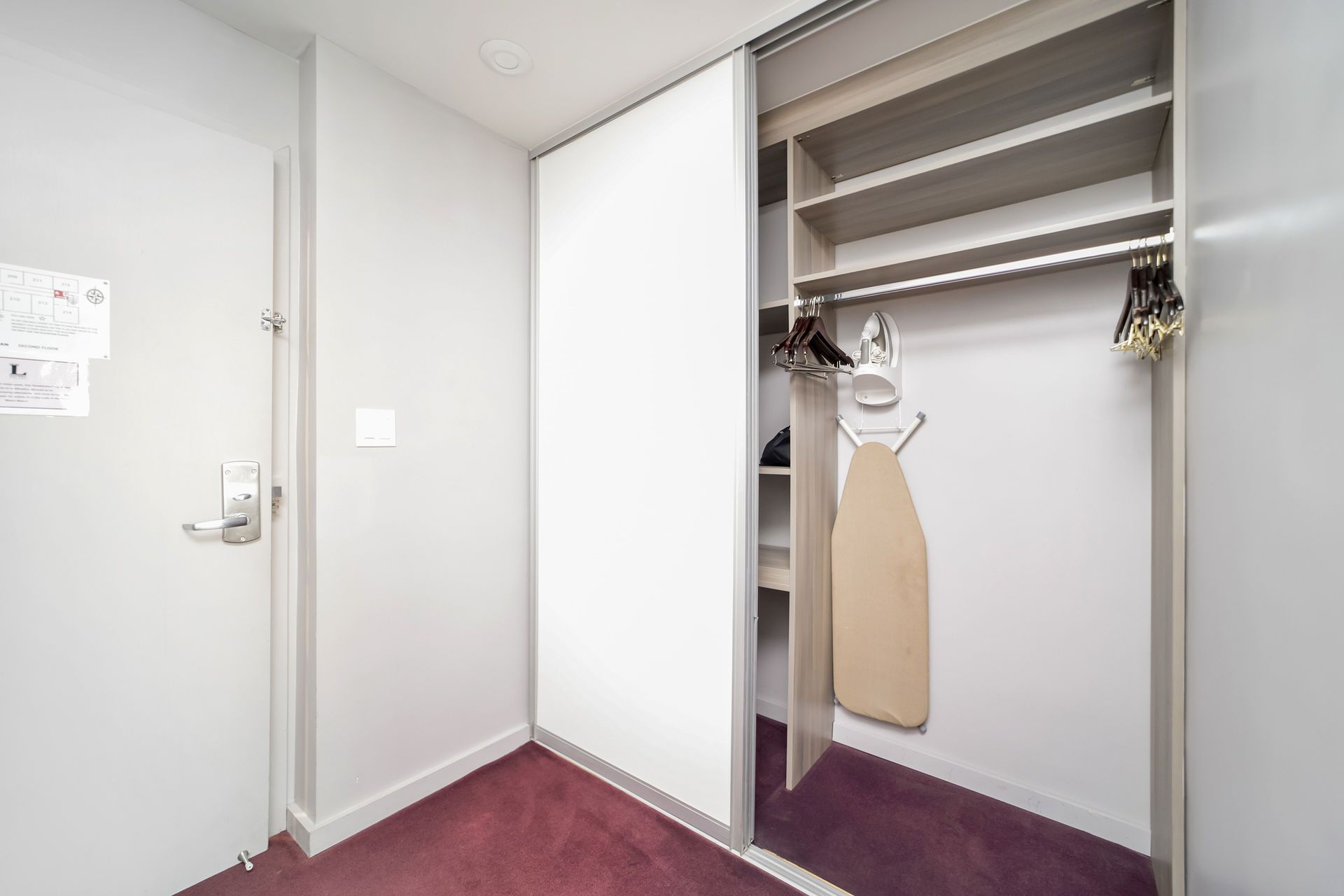 A closet with sliding doors, a hanging rod, shelves, and an ironing board.