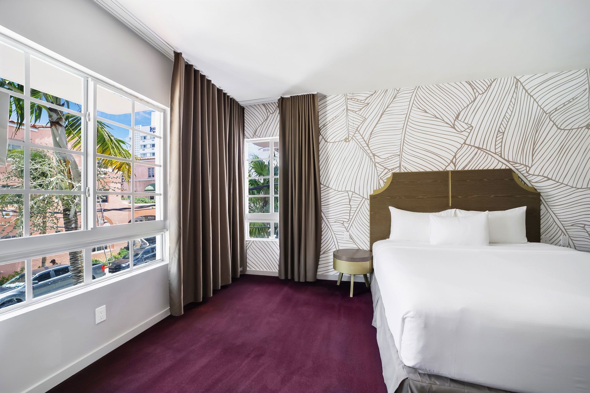 Bedroom with a bed against a patterned wall, large window with view of outside, and purple carpet.