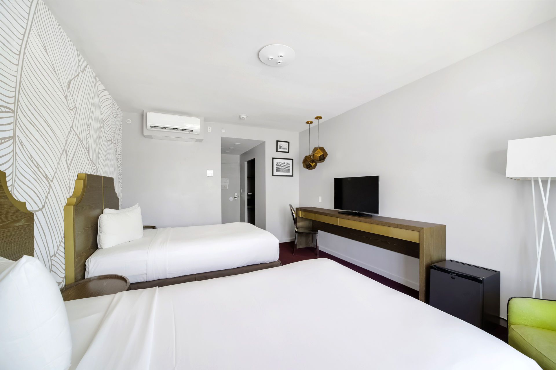 Hotel room with two beds, TV, desk, and decorative wall.