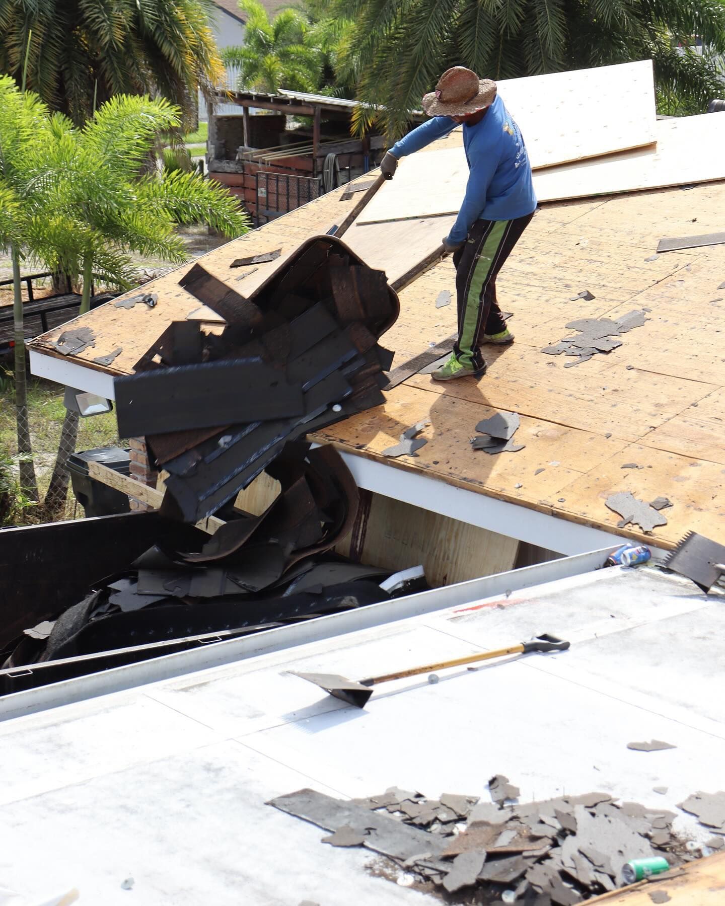 A high-angle view of a gray asphalt shingle roof on a sunny day, with a glimpse of a nearby house and backyard pool below.