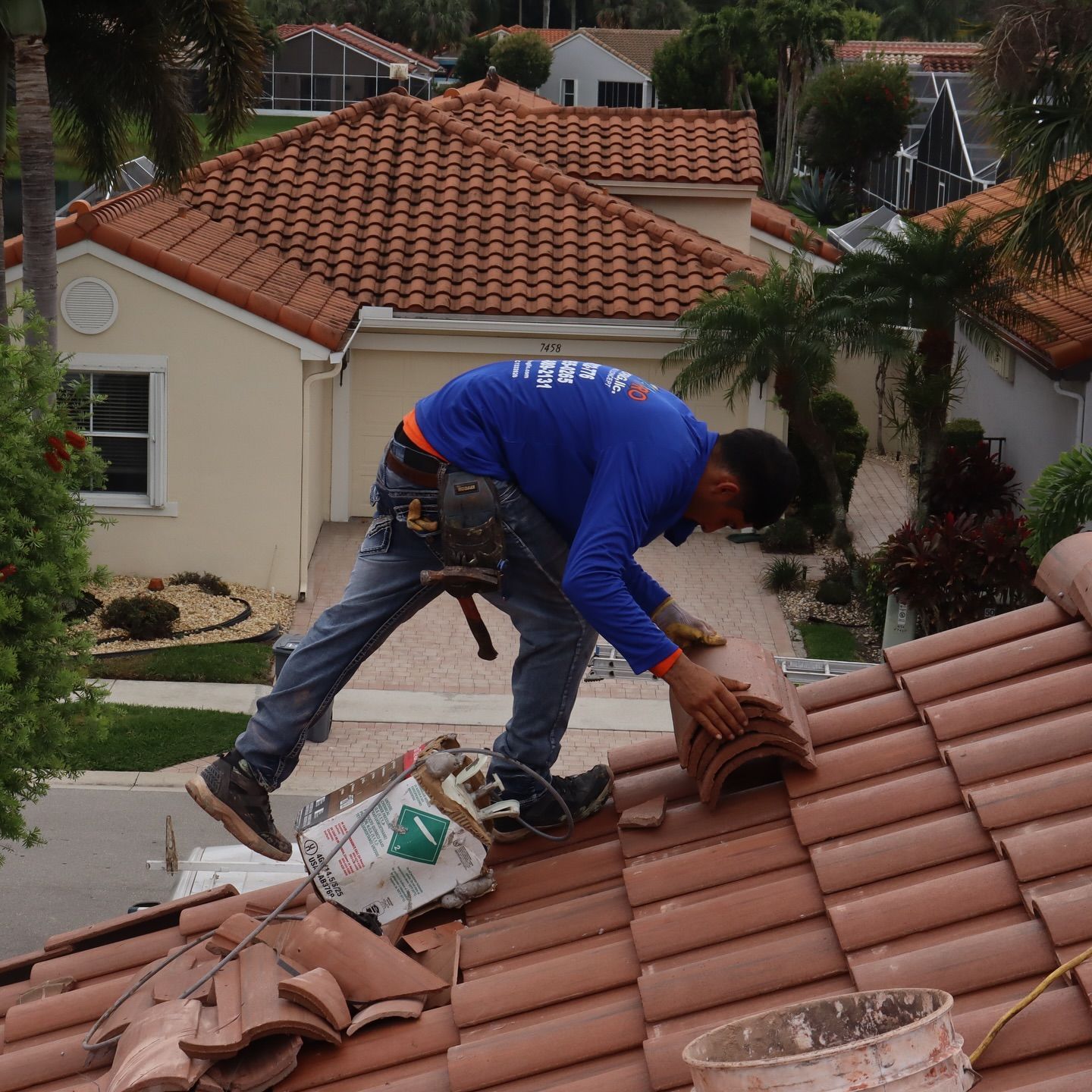 A worker in a blue long-sleeved shirt installs orange clay roof tiles on a residential home.