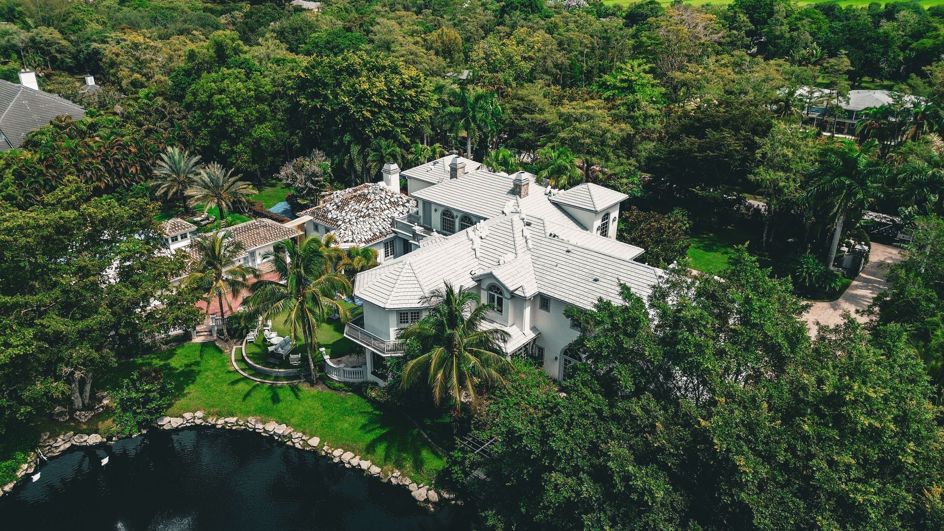 Two workers painting a white aluminum pool screen enclosure black with a spray gun, standing on a protected patio floor.