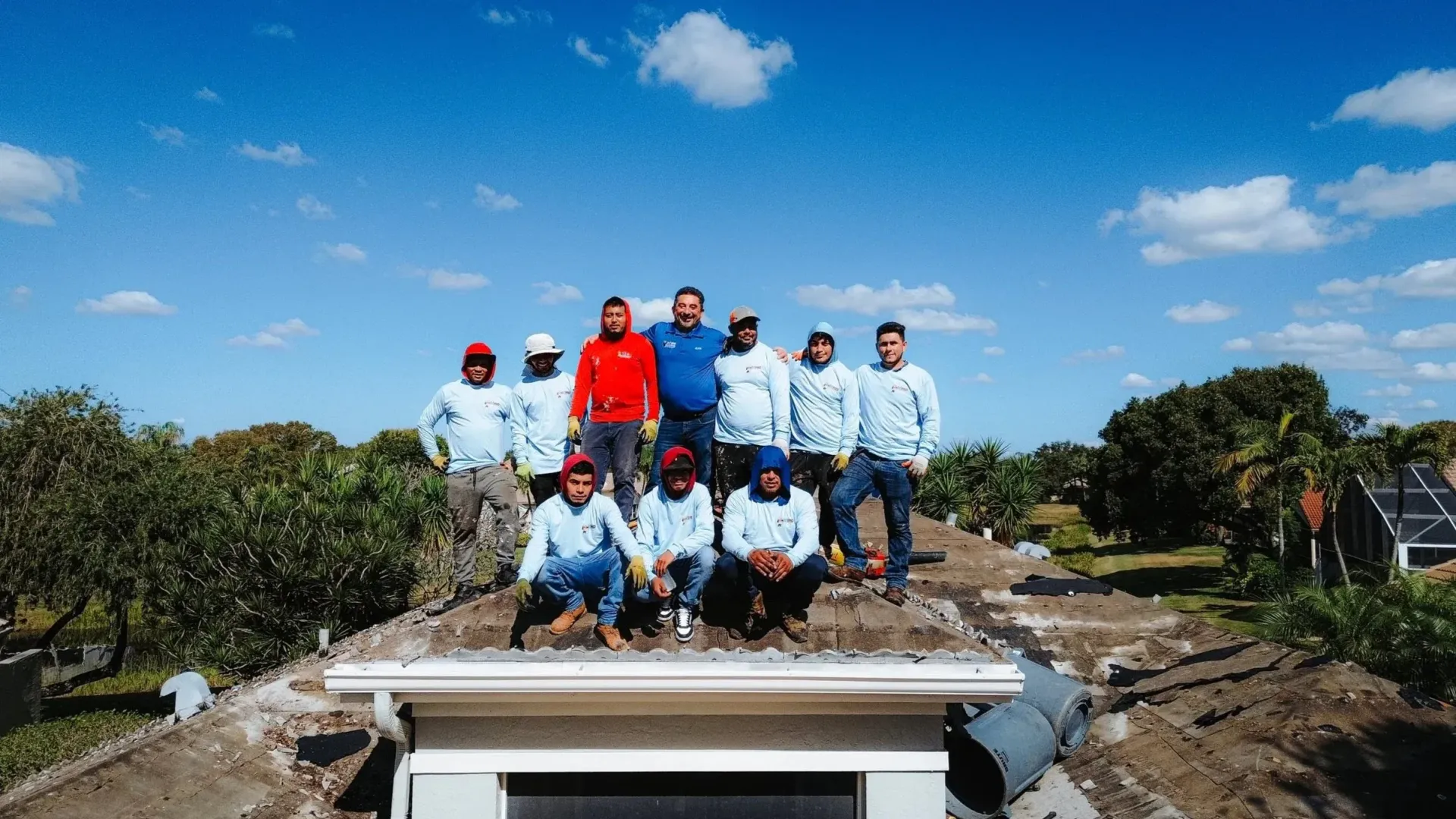A group of workers in casual clothing and work gear stand together on a flat roof under a clear blue sky.