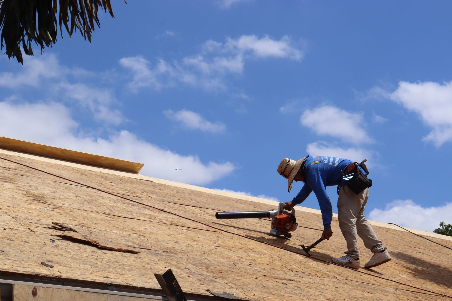 A partially constructed two-story house with exterior framing, white protective wrap, and gray shingled roof under blue sky.