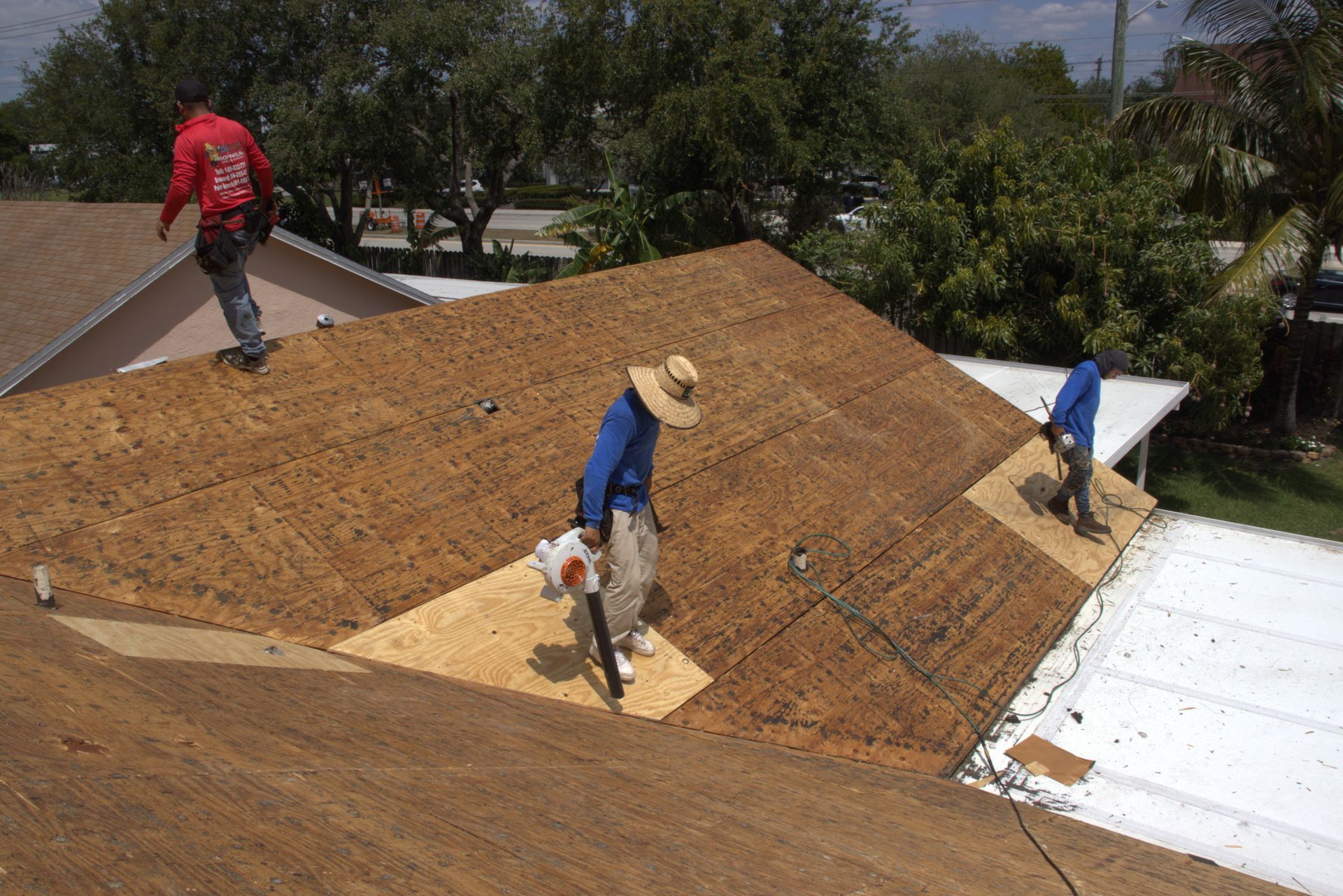 A person stands on a ladder cleaning a chimney on a tiled roof.