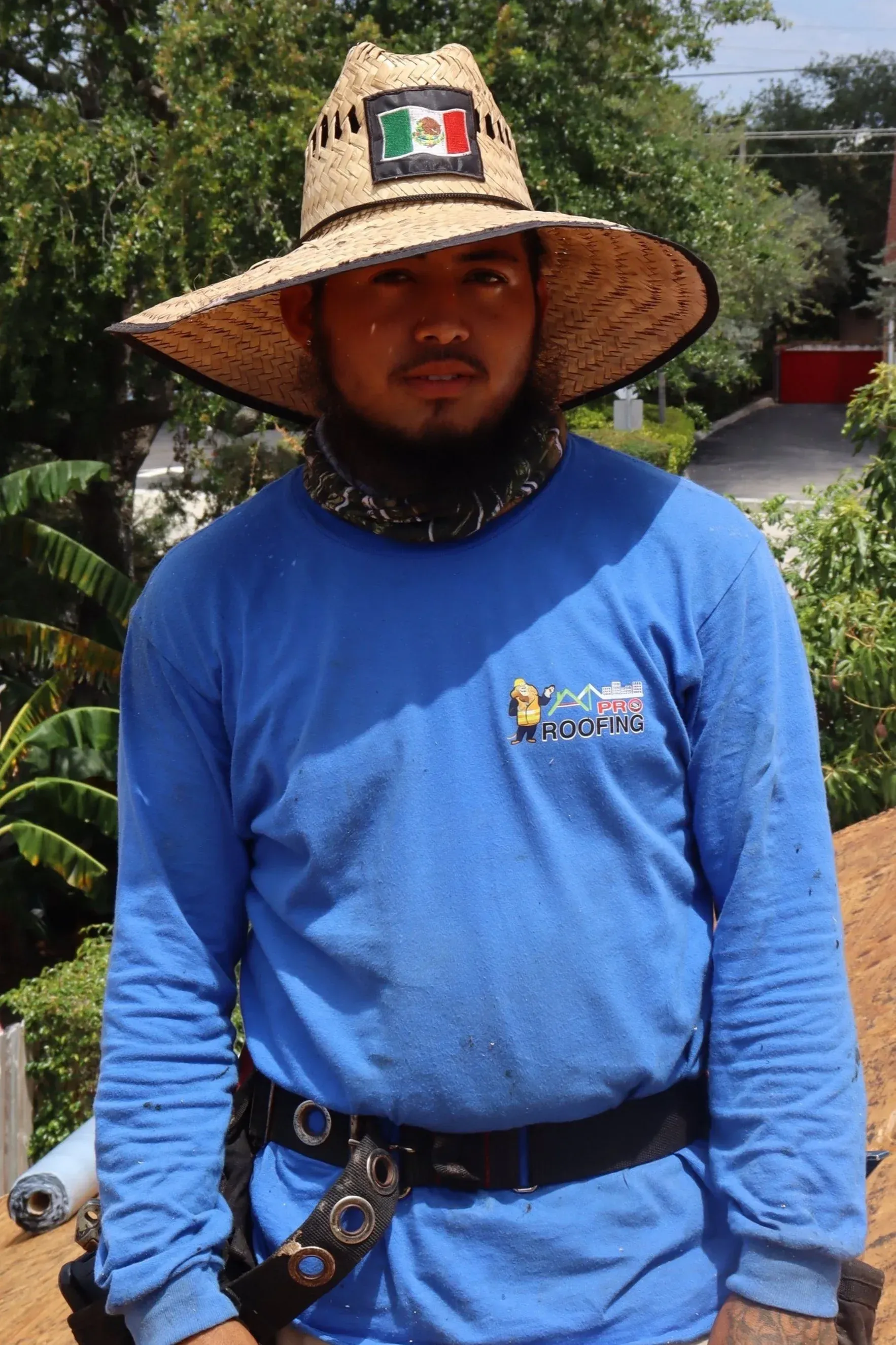 A person wearing a straw hat with a Mexican flag patch and a blue long-sleeved shirt, standing outdoors.