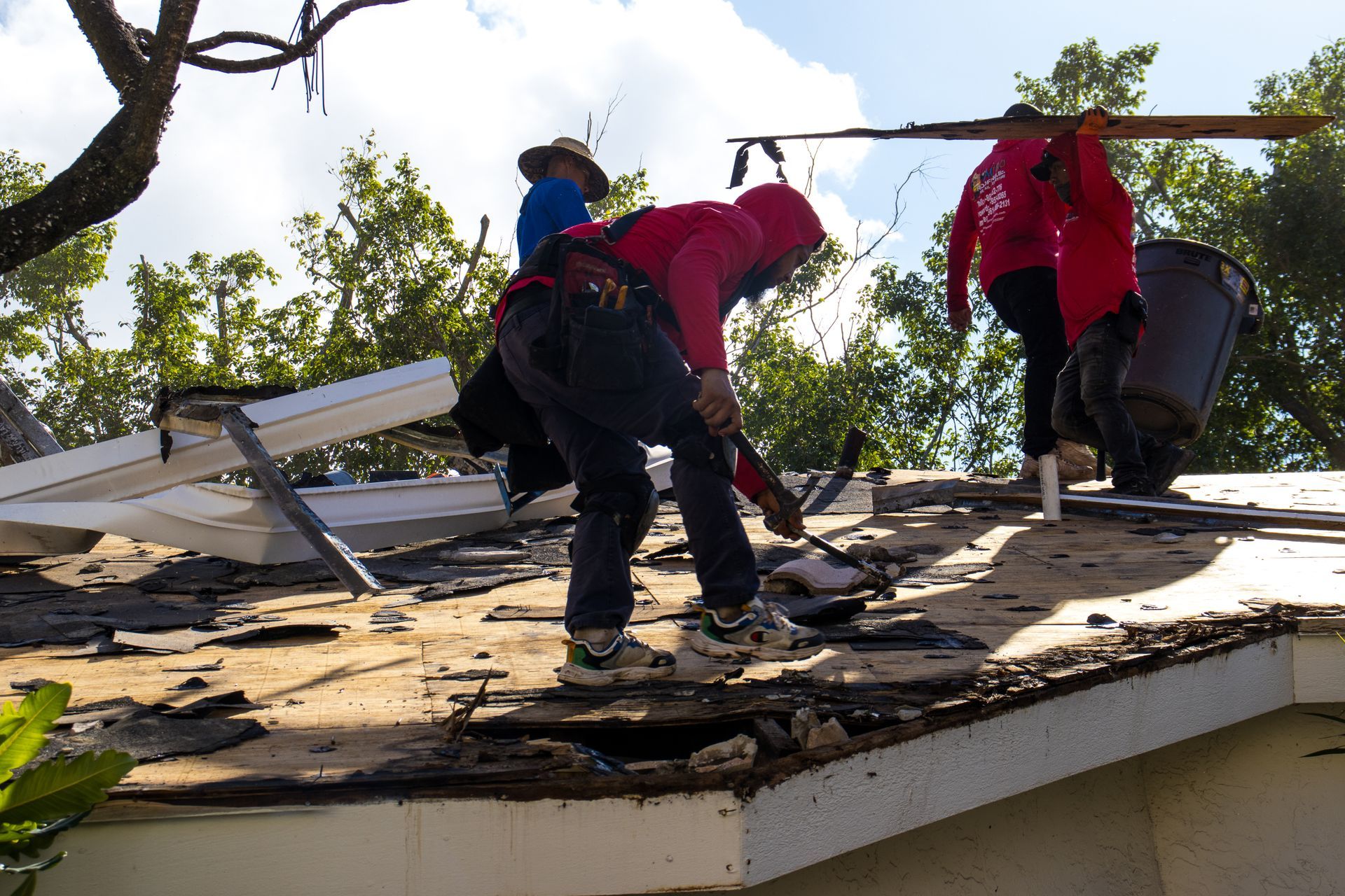 A person stands on a ladder cleaning a chimney on a tiled roof.