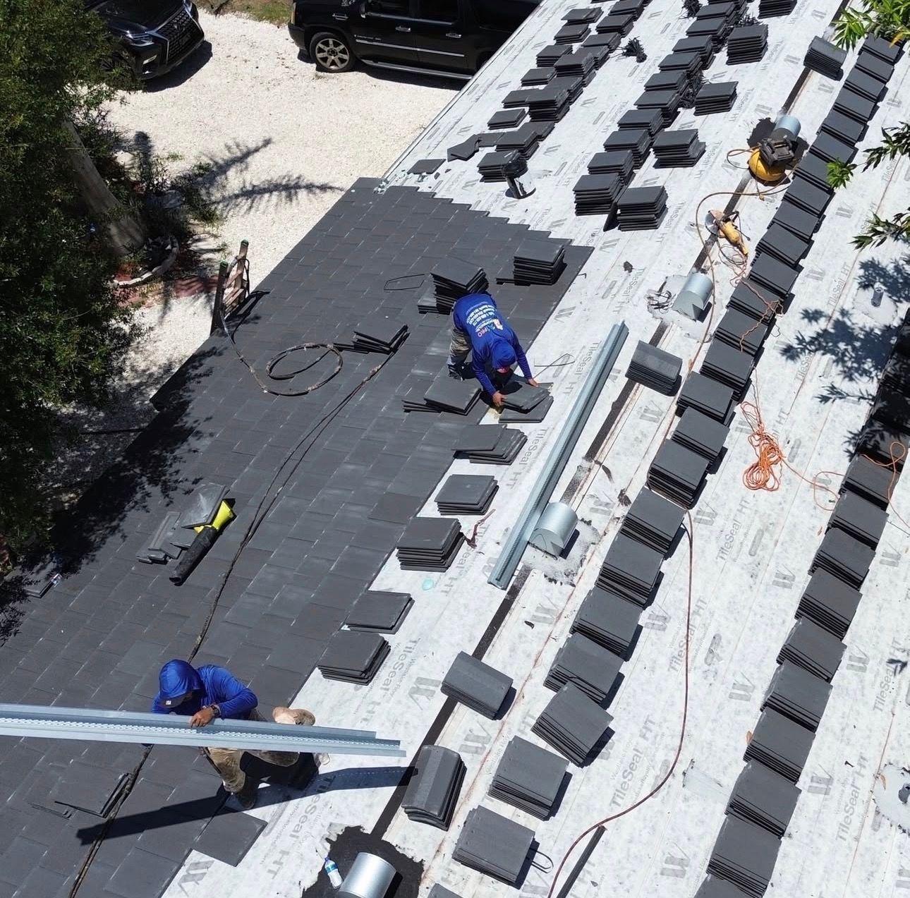 Workers apply expanding foam adhesive to secure clay roof tiles during construction.