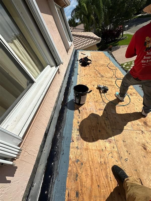 A worker uses a spray foam gun to adhere terracotta roof tiles to an underlayment on a sloping roof.