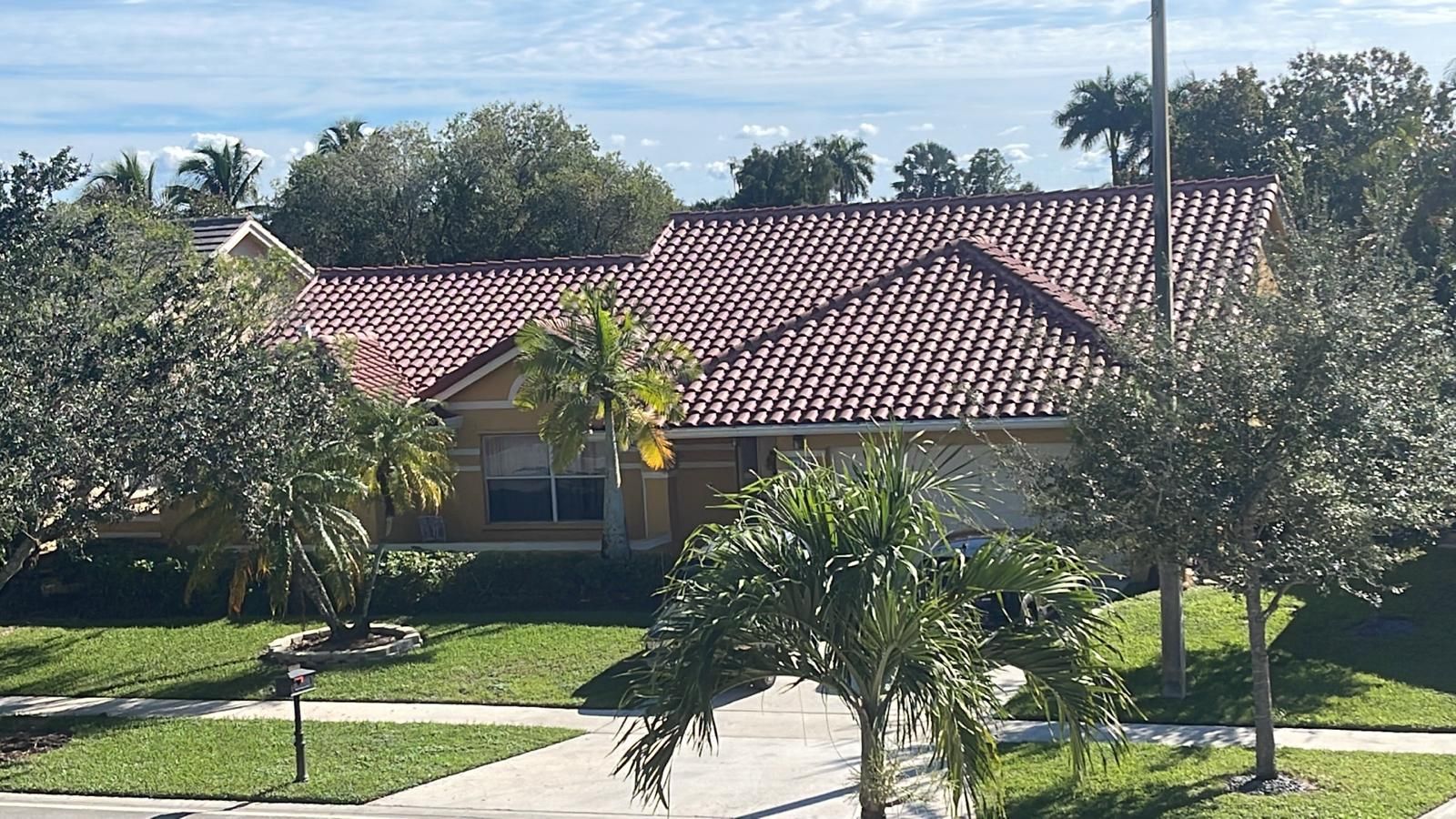 A worker in a blue shirt and hat uses a shovel to remove old roof shingles into a chute on a sunny, residential roof.