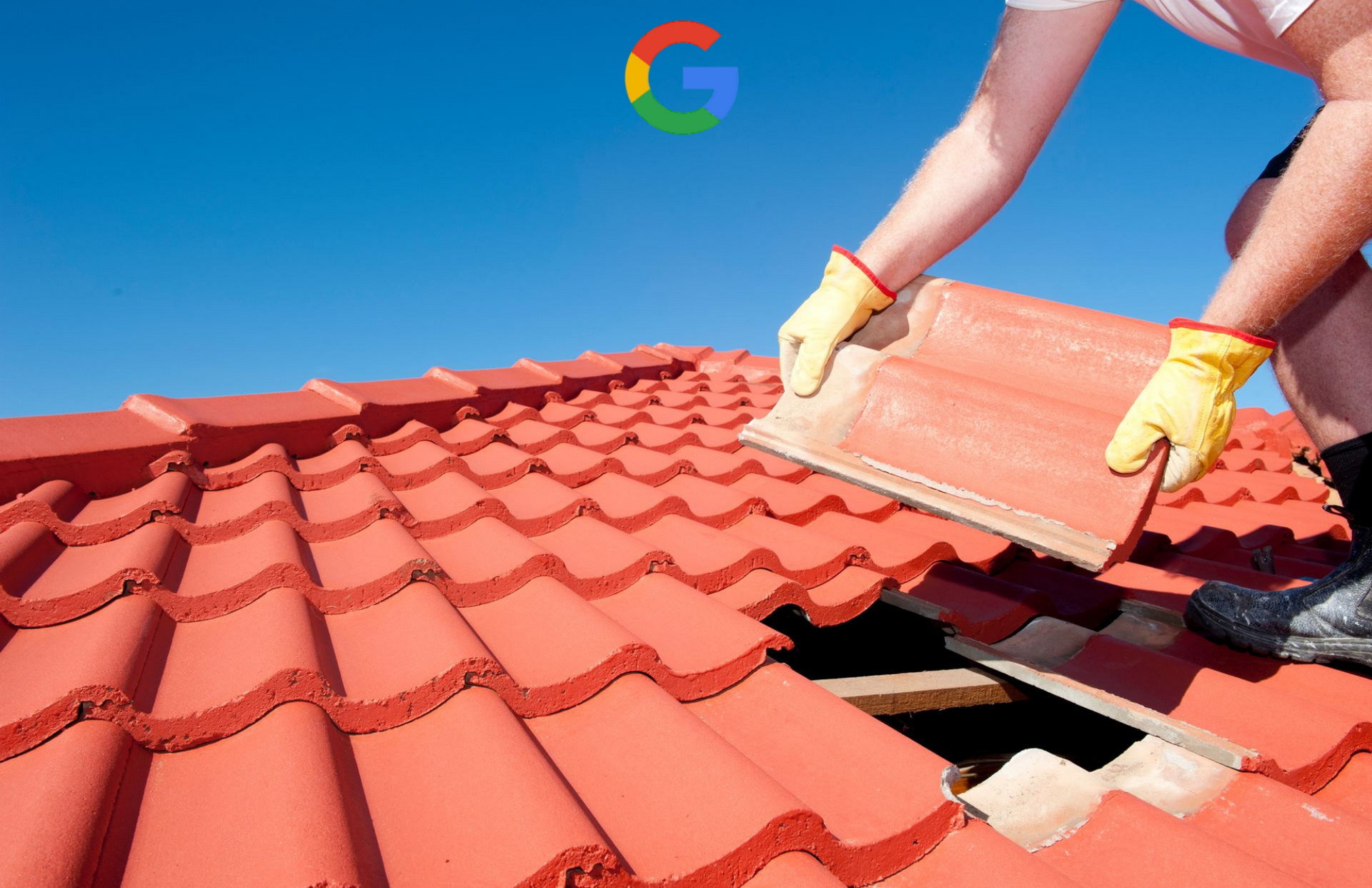 A worker wearing yellow gloves installs a red clay tile onto a roof under a clear blue sky.