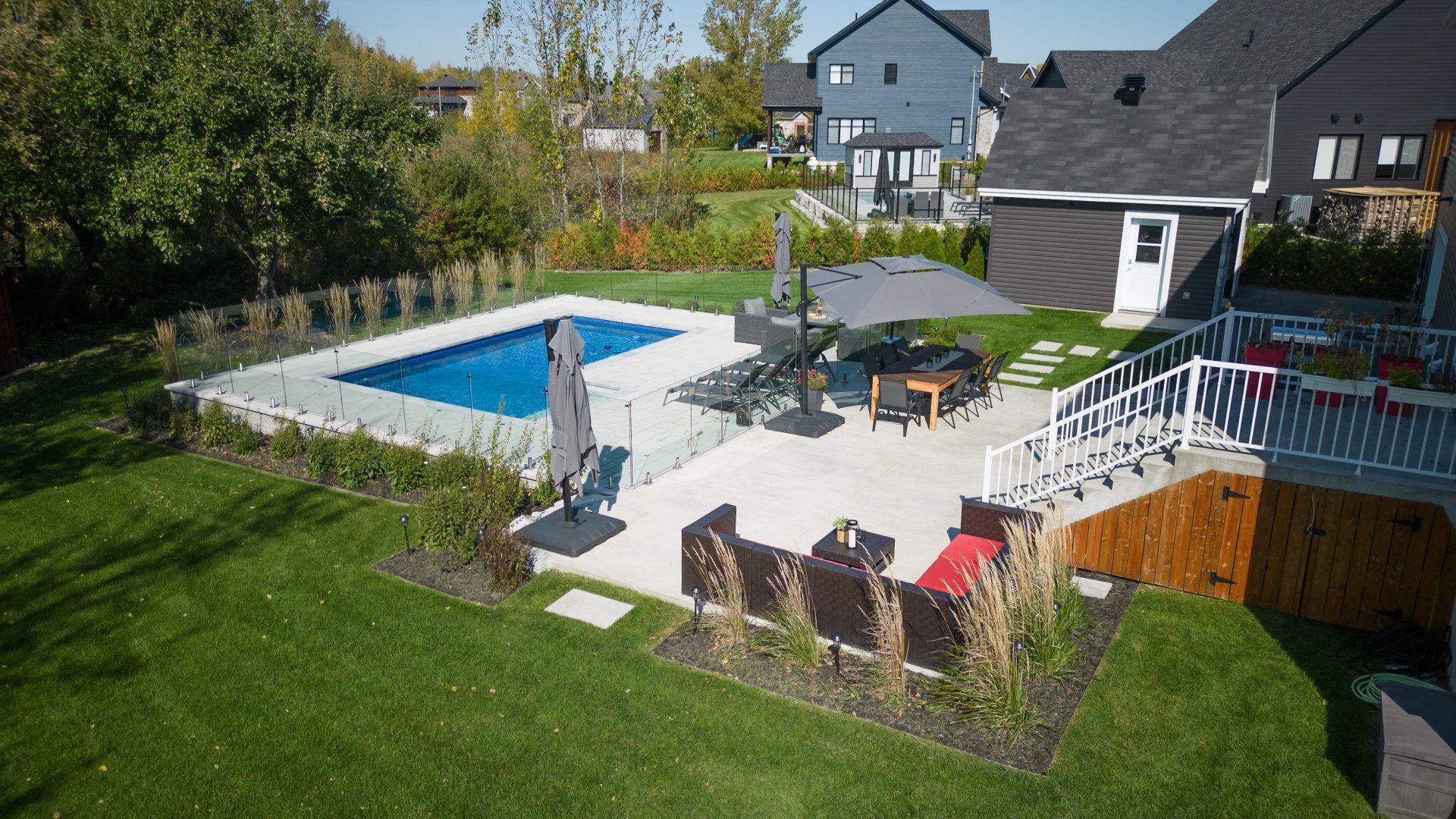 Deux chaises longues et une petite table sous un grand parasol beige déporté sur une terrasse ensoleillée au bord d'une piscine.
