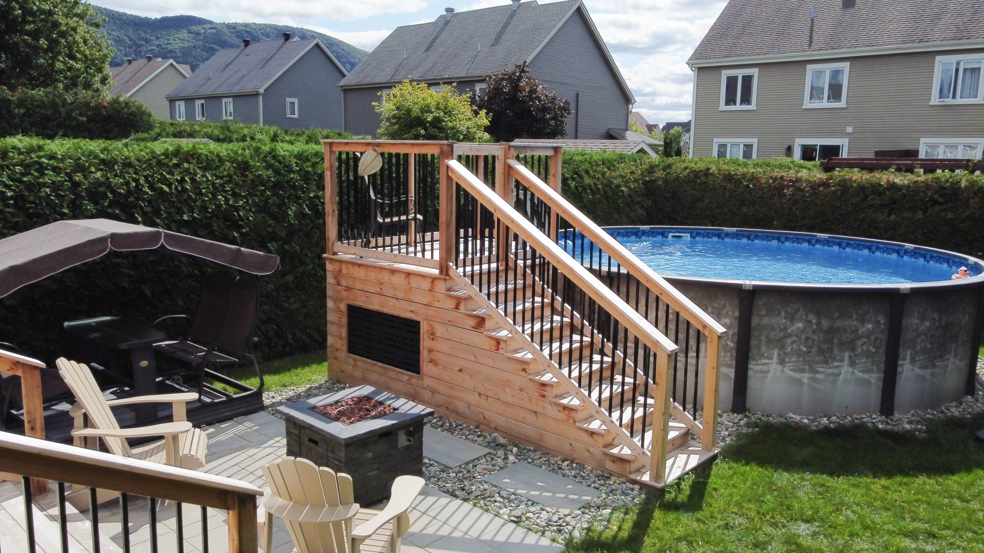 La cour arrière comprend une piscine avec une terrasse en bois et des escaliers, à côté d'un coin salon avec un foyer et une balançoire.