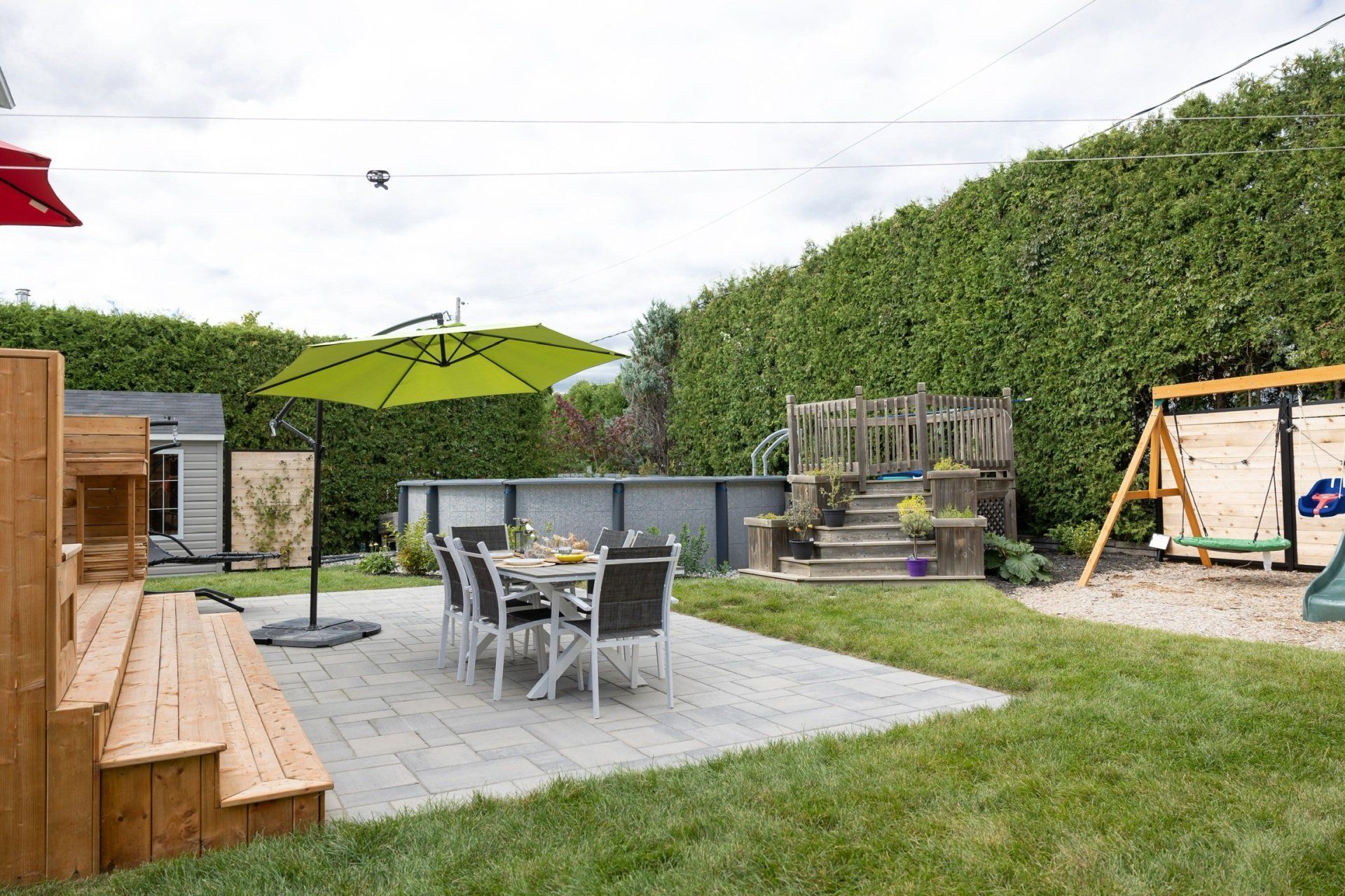 Une piscine dans un jardin avec une eau bleu clair, des meubles de terrasse gris et deux grands parasols adossés à une clôture grise.