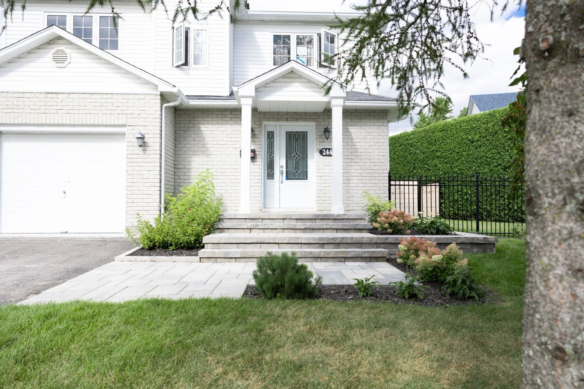 Une maison de banlieue en pierre claire, avec une porte d'entrée blanche, des marches en pierre et une pelouse paysagée.
