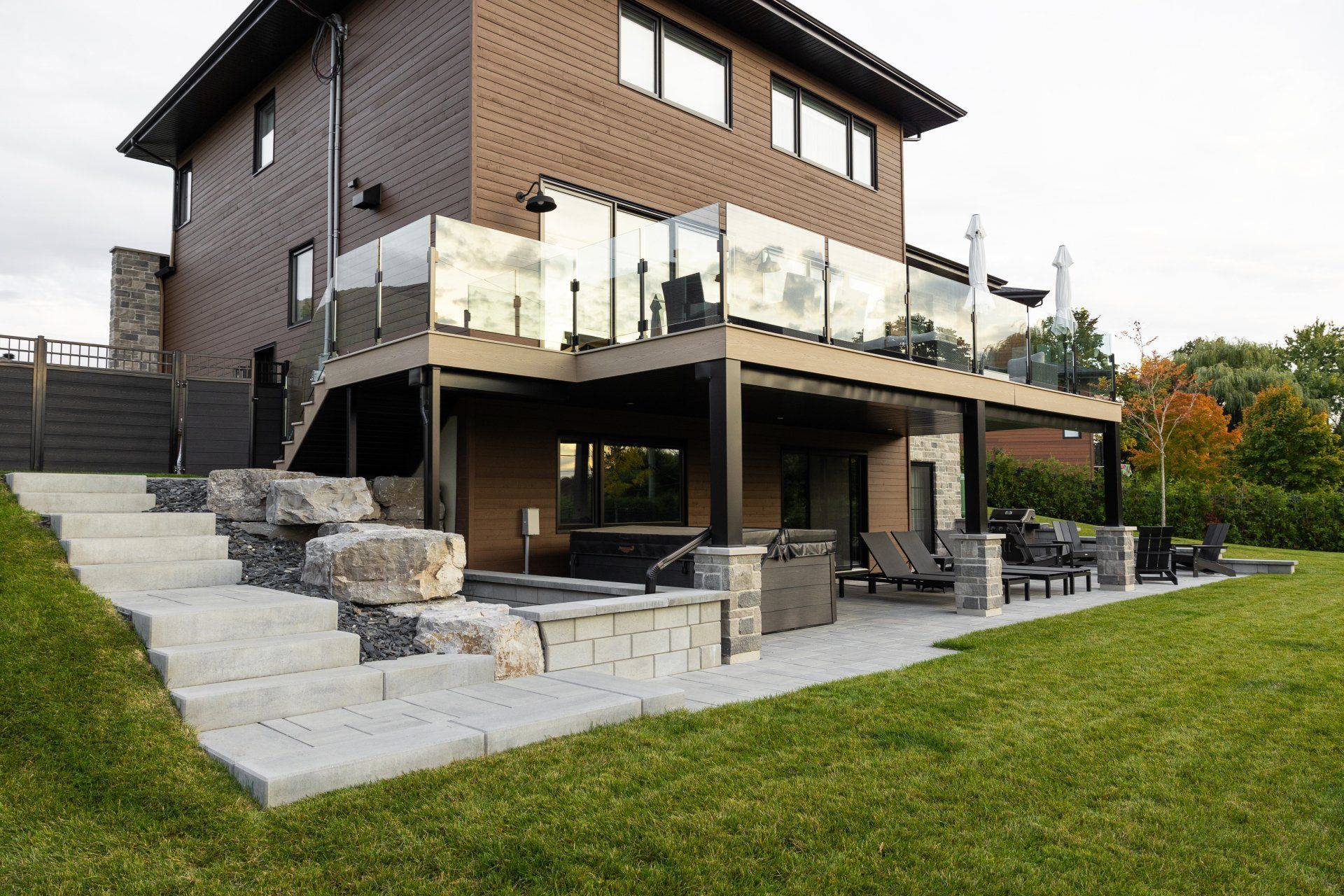 Une maison moderne en briques avec une terrasse surélevée dotée de balustrades en verre, d'un escalier en pierre et d'un patio pavé.