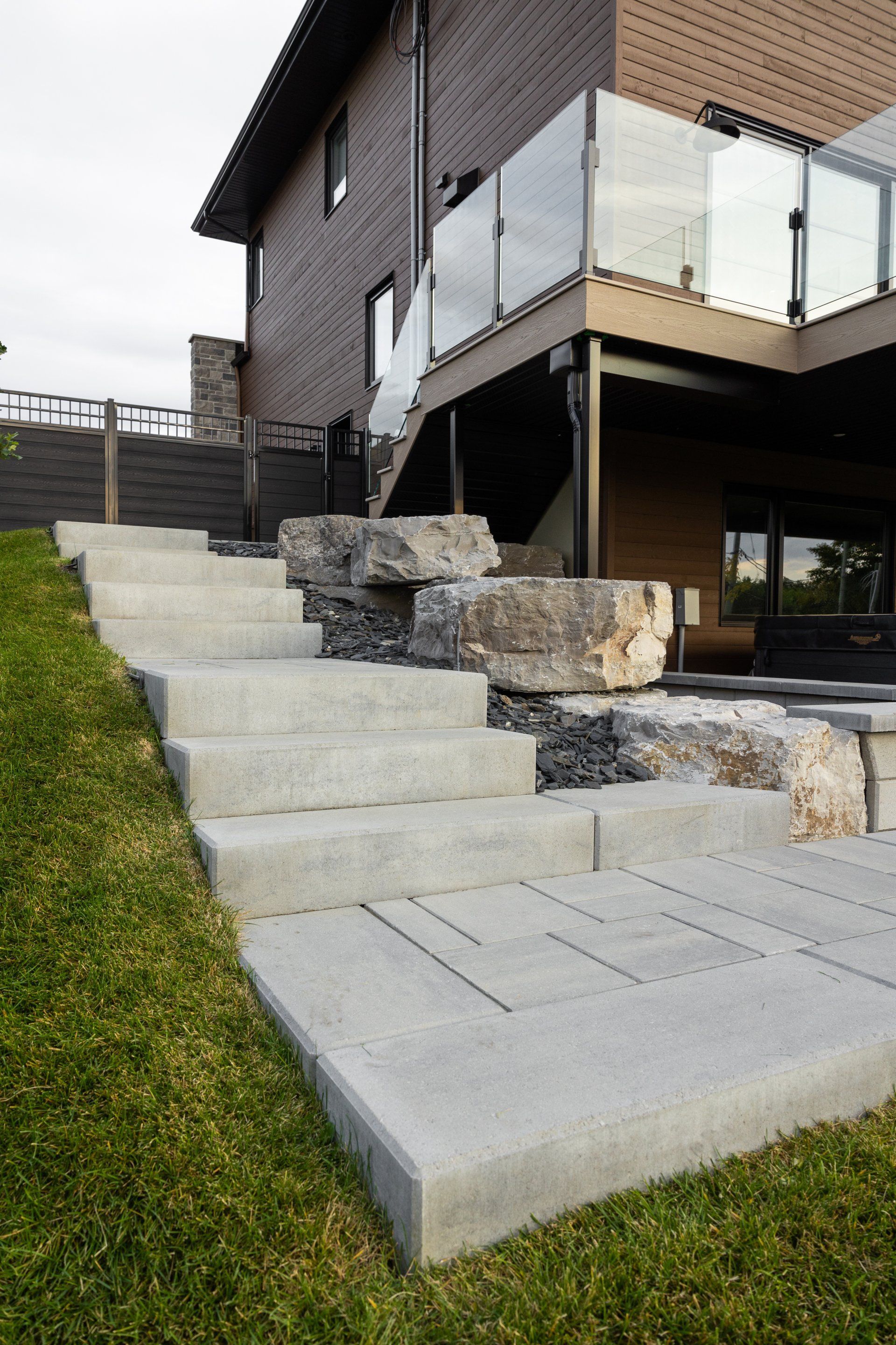 Un escalier en pierre mène à une terrasse moderne dotée d'une balustrade en verre, fixée sur le côté de la maison.