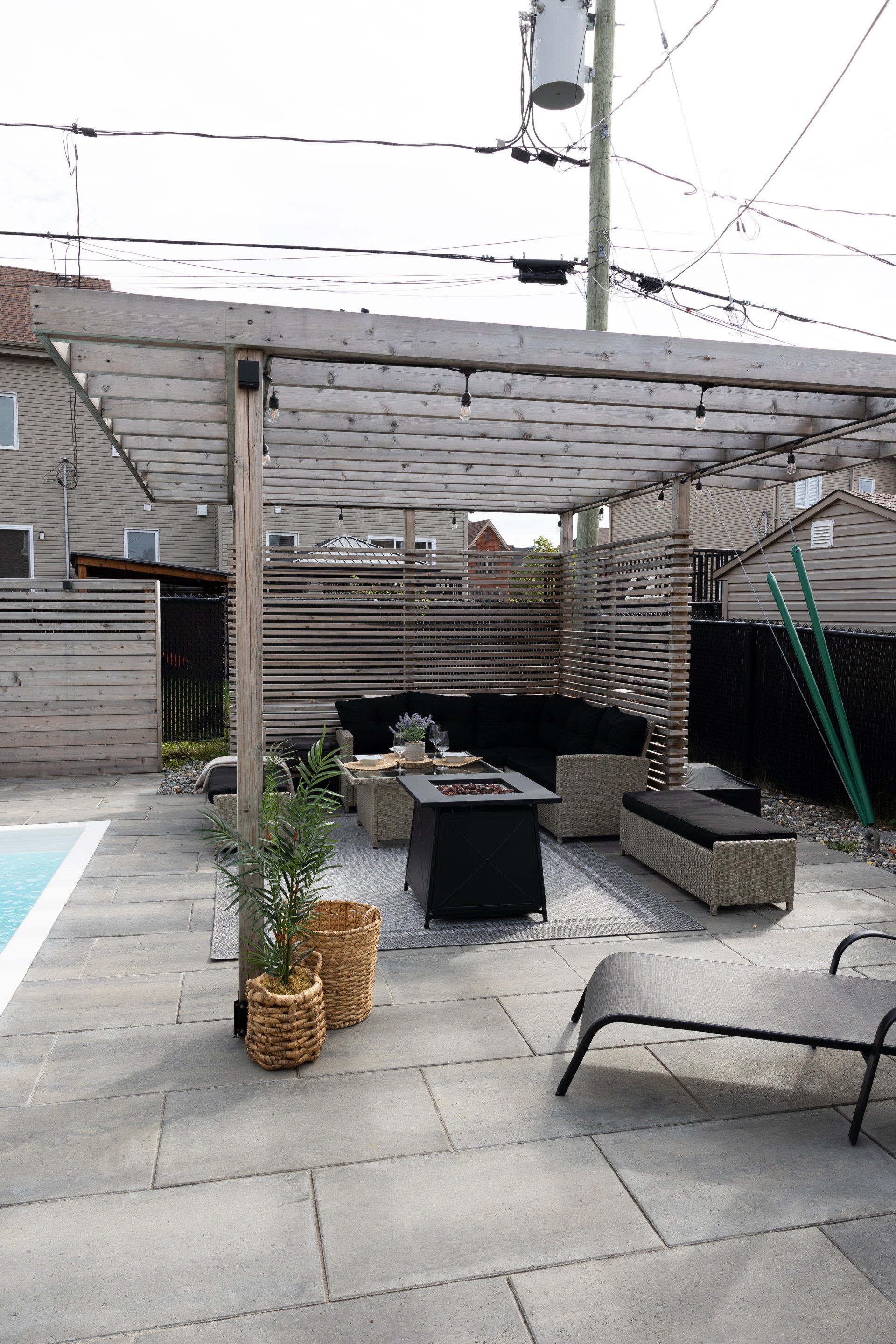 Une terrasse arrière avec une pergola, un canapé d'angle extérieur, un foyer et une chaise longue près d'une piscine.