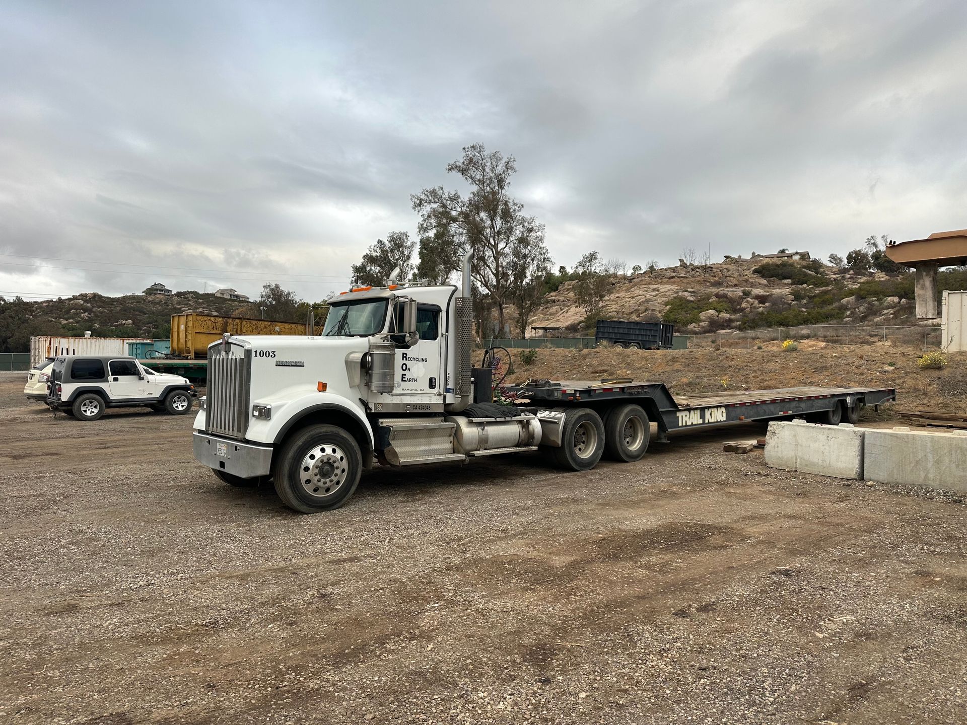 A white semi truck with a flatbed trailer is parked in a gravel lot.