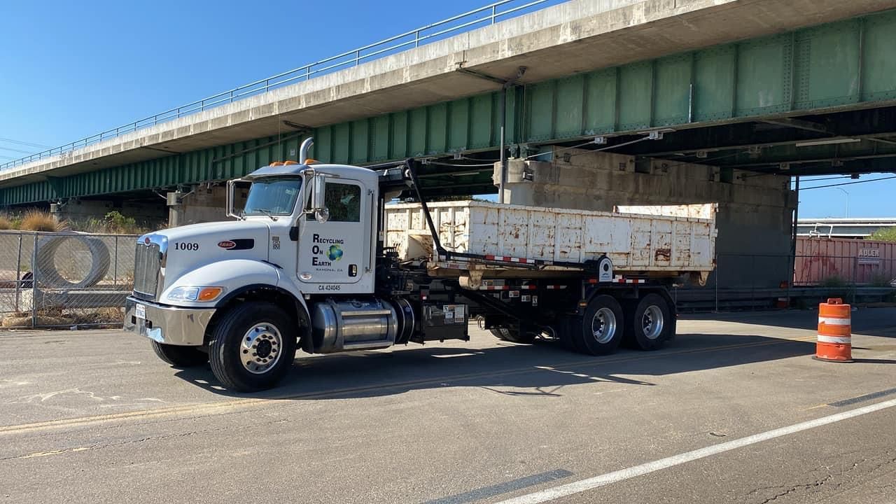 A dump truck is parked under a bridge in a parking lot.