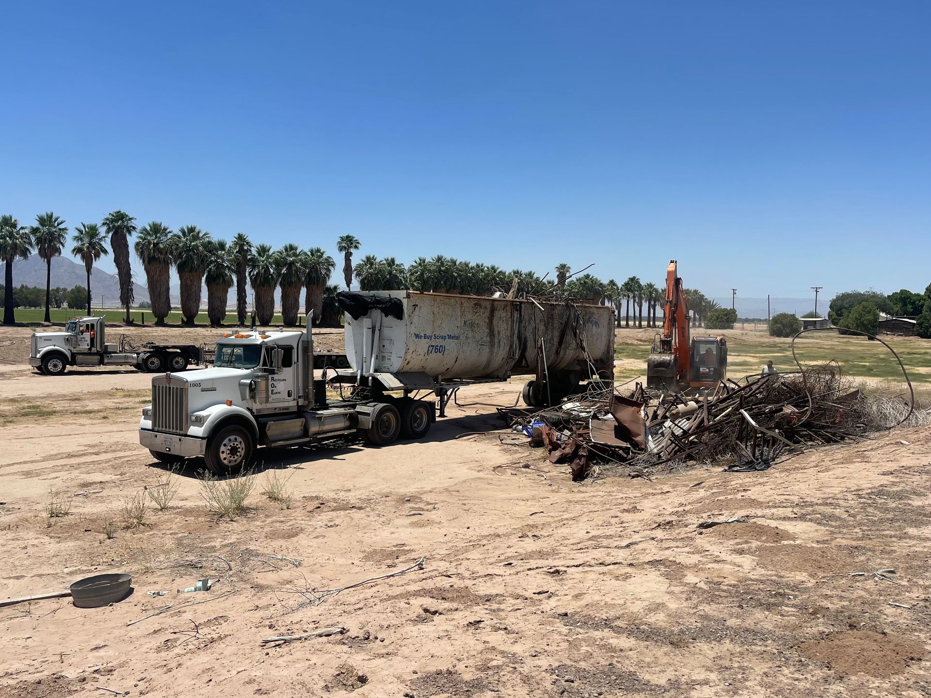 A dump truck is parked in a dirt field with palm trees in the background