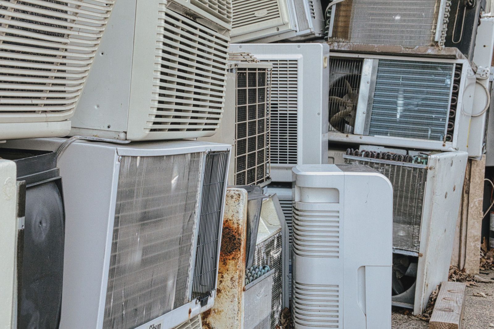 Pile of discarded window air conditioners, mostly white, stacked outdoors.