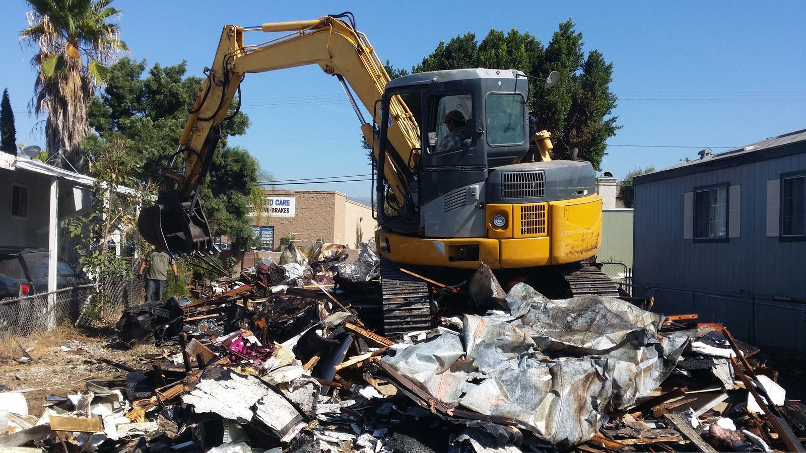 A yellow excavator is demolishing a mobile home