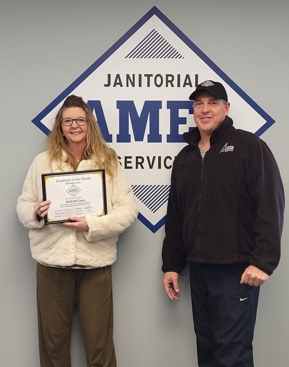 Woman holds certificate next to man in front of AME Janitorial Service logo.