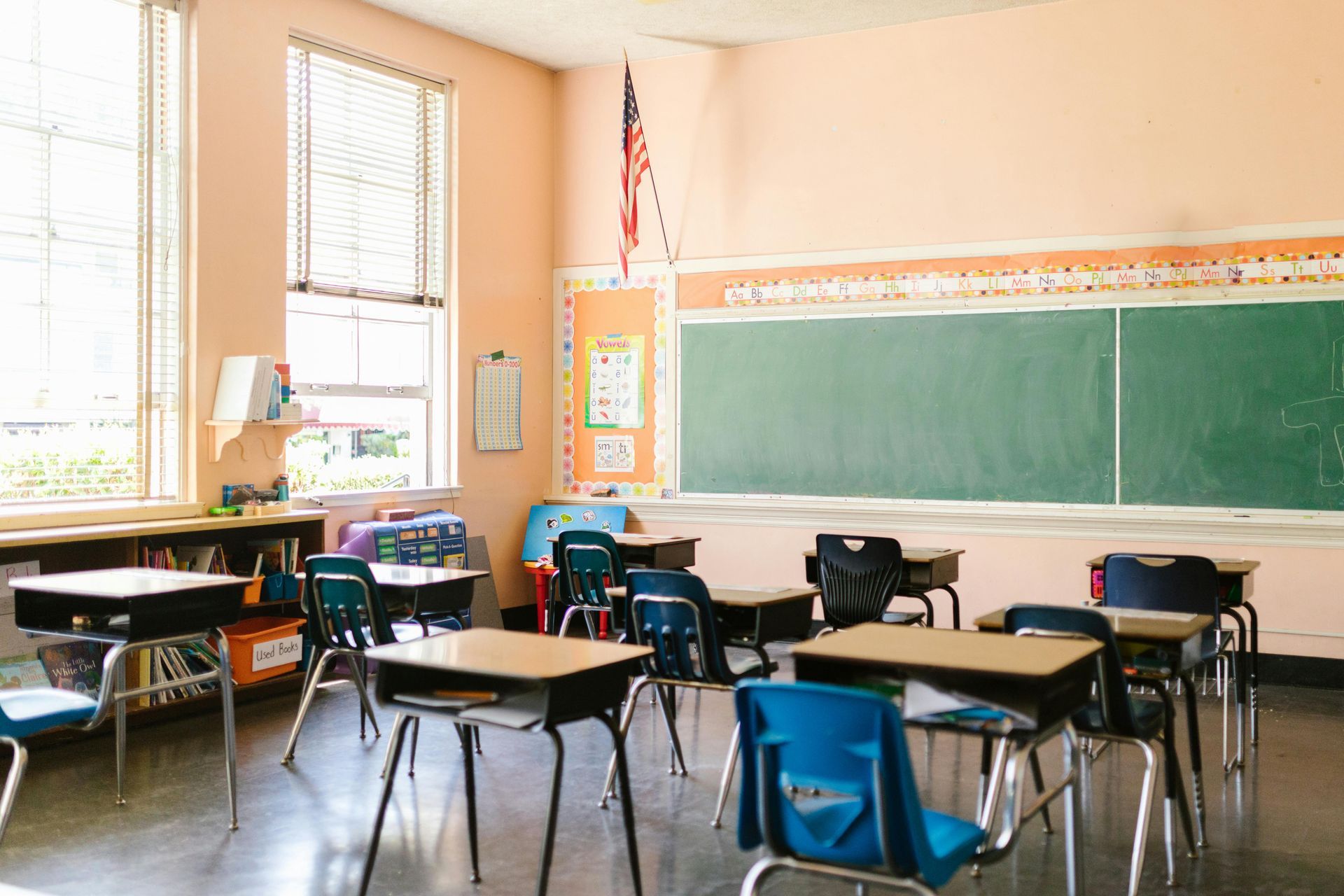 Empty school classroom with desks, a chalkboard, and American flag.