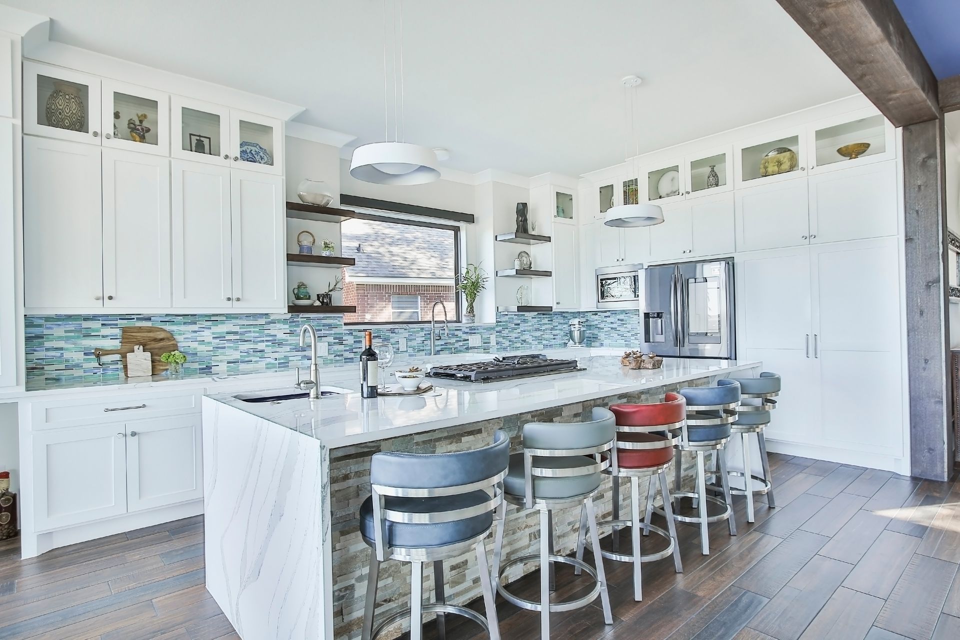 A kitchen with white cabinets , a large island , stools and a refrigerator.